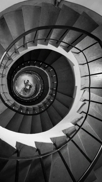 Black and white image looking down a large spiral staircase to man at the bottom in running stance