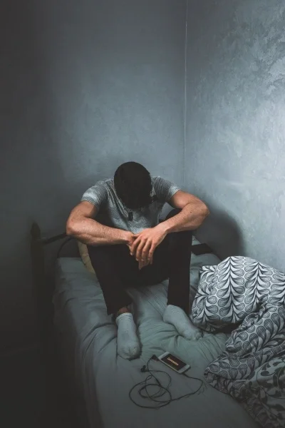 Man sitting on twin bed hunched over looking down