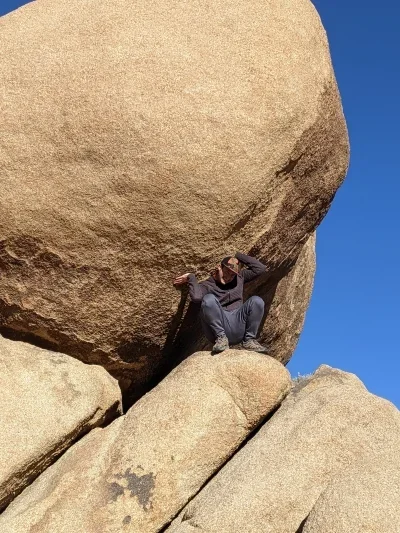 Person posing under huge boulder as if they're holding it up