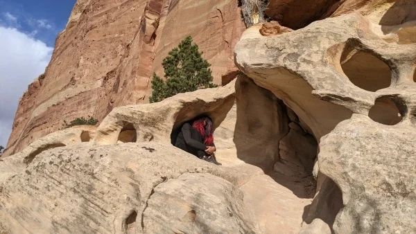 Person crouched in a small opening in a rock