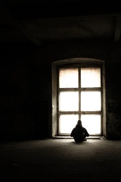 Silhouette of a person sitting in front of a window in an abandoned industrial space