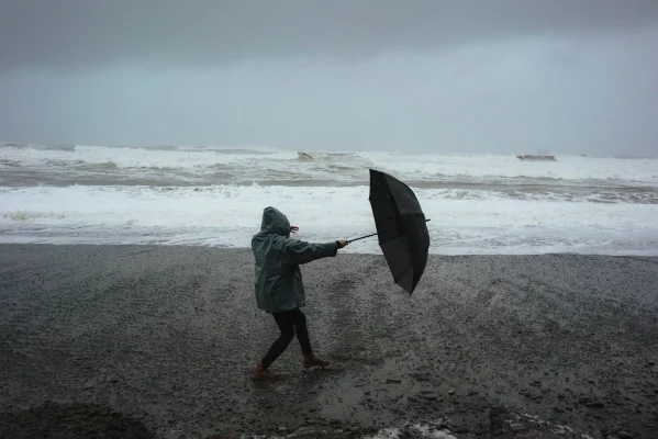 Person struggles to hold umbrella on the beach on a gray day