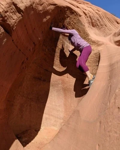 Woman using hands and feet to brace climb a red rock feature