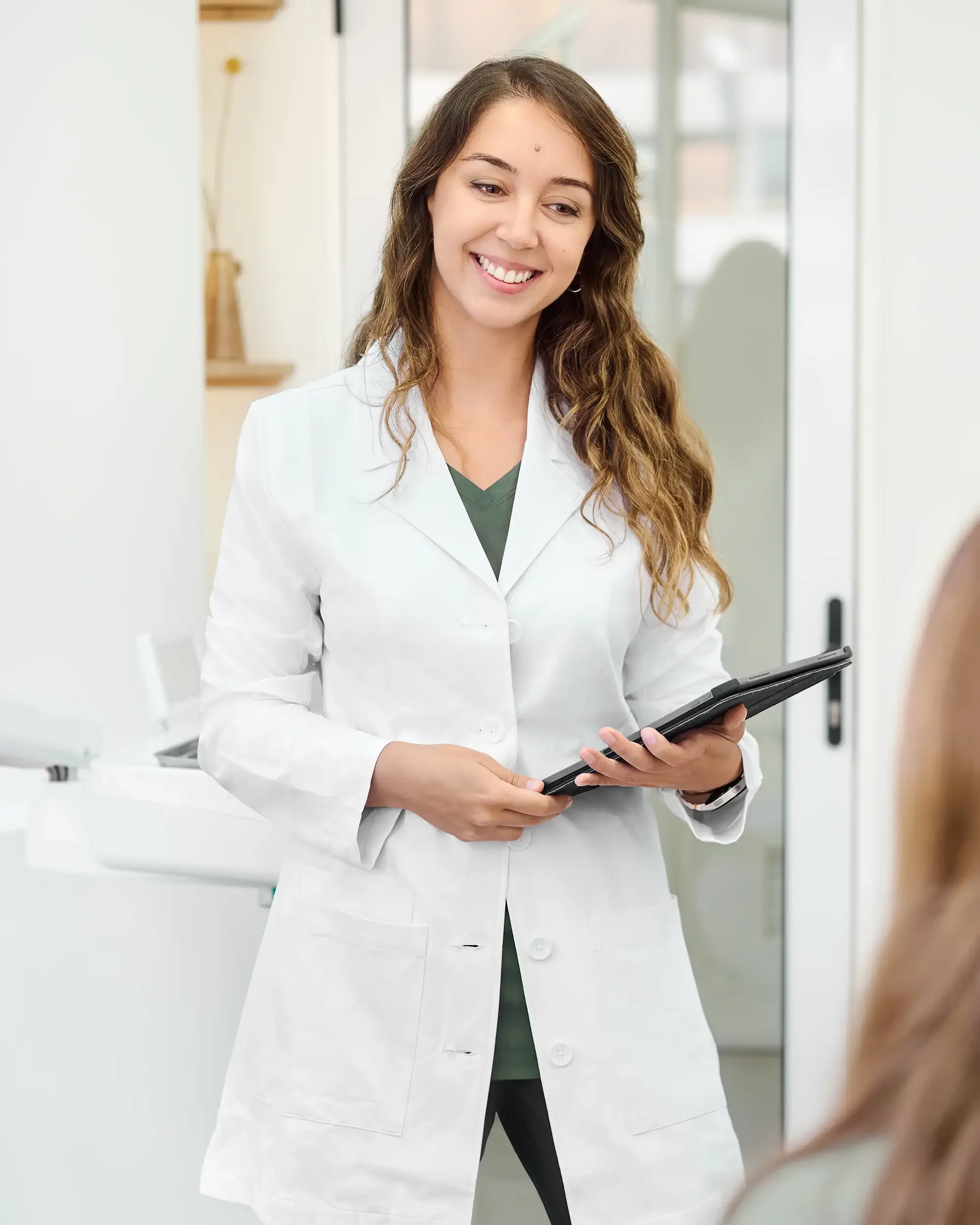 Dentista con bata blanca y una tablet sonriendo a paciente en Clínica Aires, clínica dental en Providencia.
