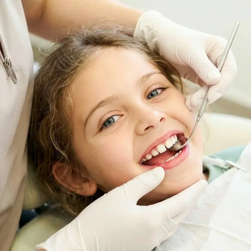 Niña sonriendo a cámara mientras la atienden manos de dentista  en Clínica Aires