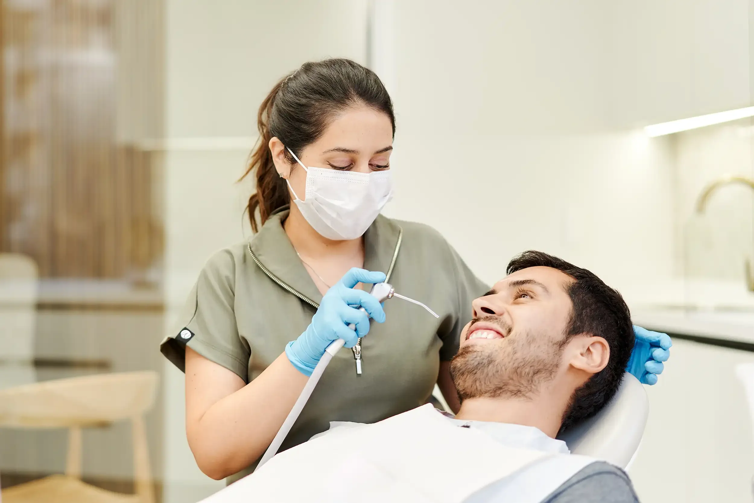 Cirujana dentista aplica tratamiento periodontal, acerca jeringa triple a paciente hombre en Clínica Aires