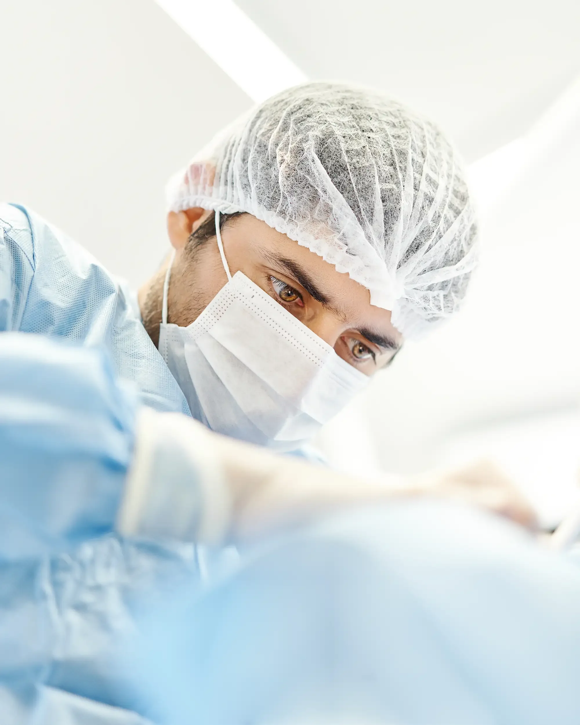 Dentista realizando una cirugía en una clínica dental en Providencia, usa gorro, mascarilla y bata de color azul, con enfoque en su rostro concentrado.