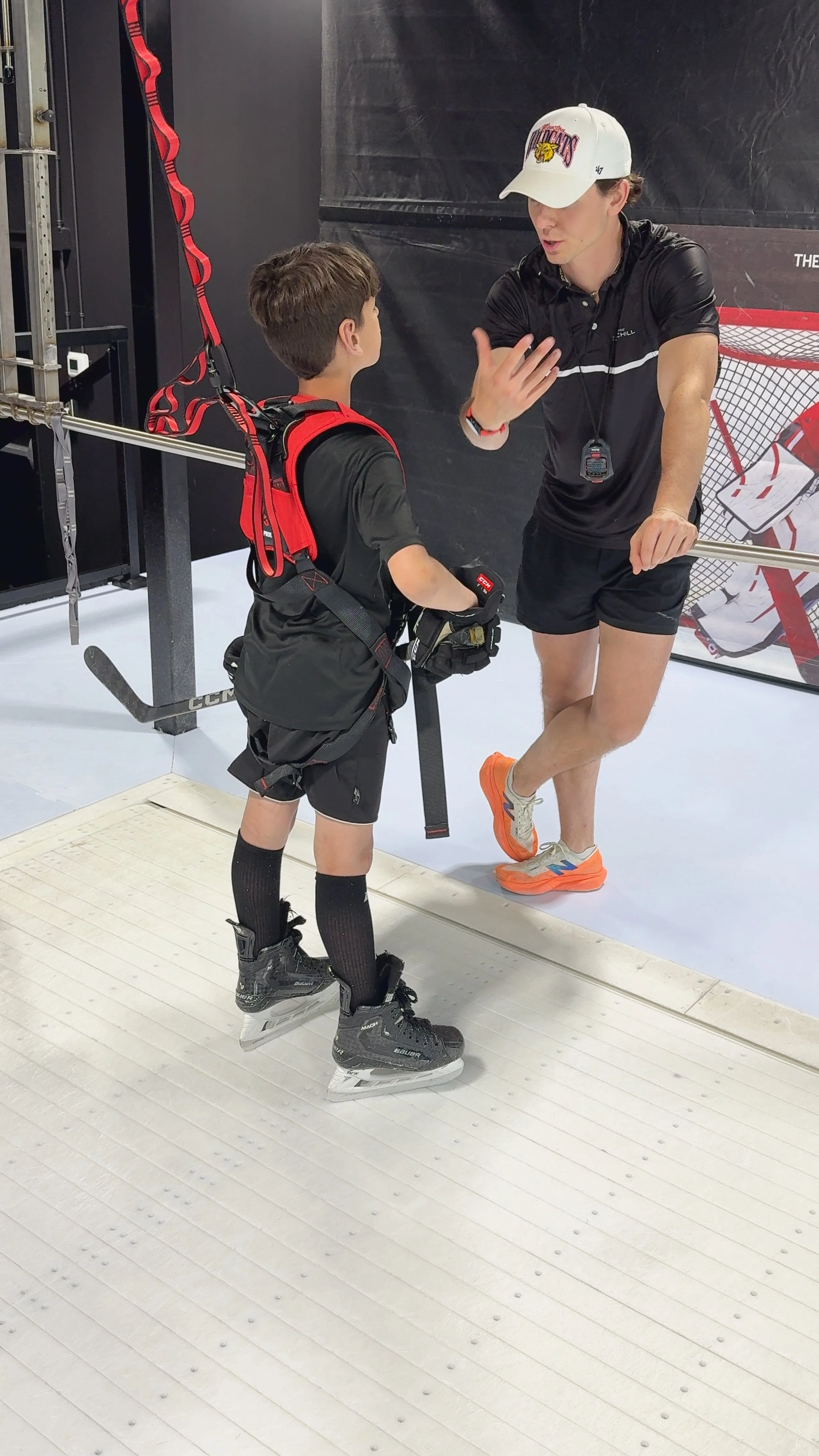 Young hockey player in black uniform and ice skates listening to coach on ice rink