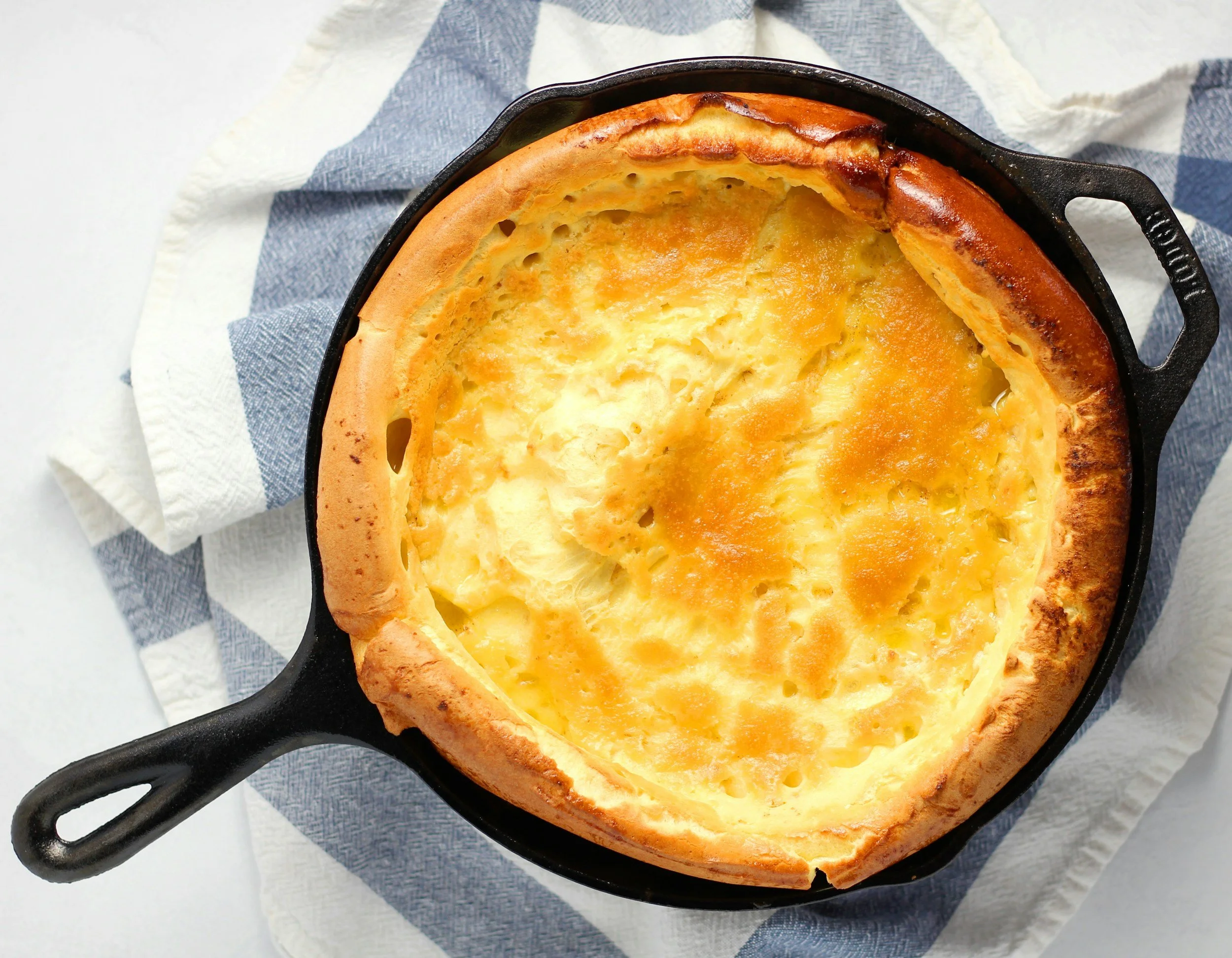 A baked cheese bread in a cast iron skillet with a golden crust, resting on white and blue cloth napkins.