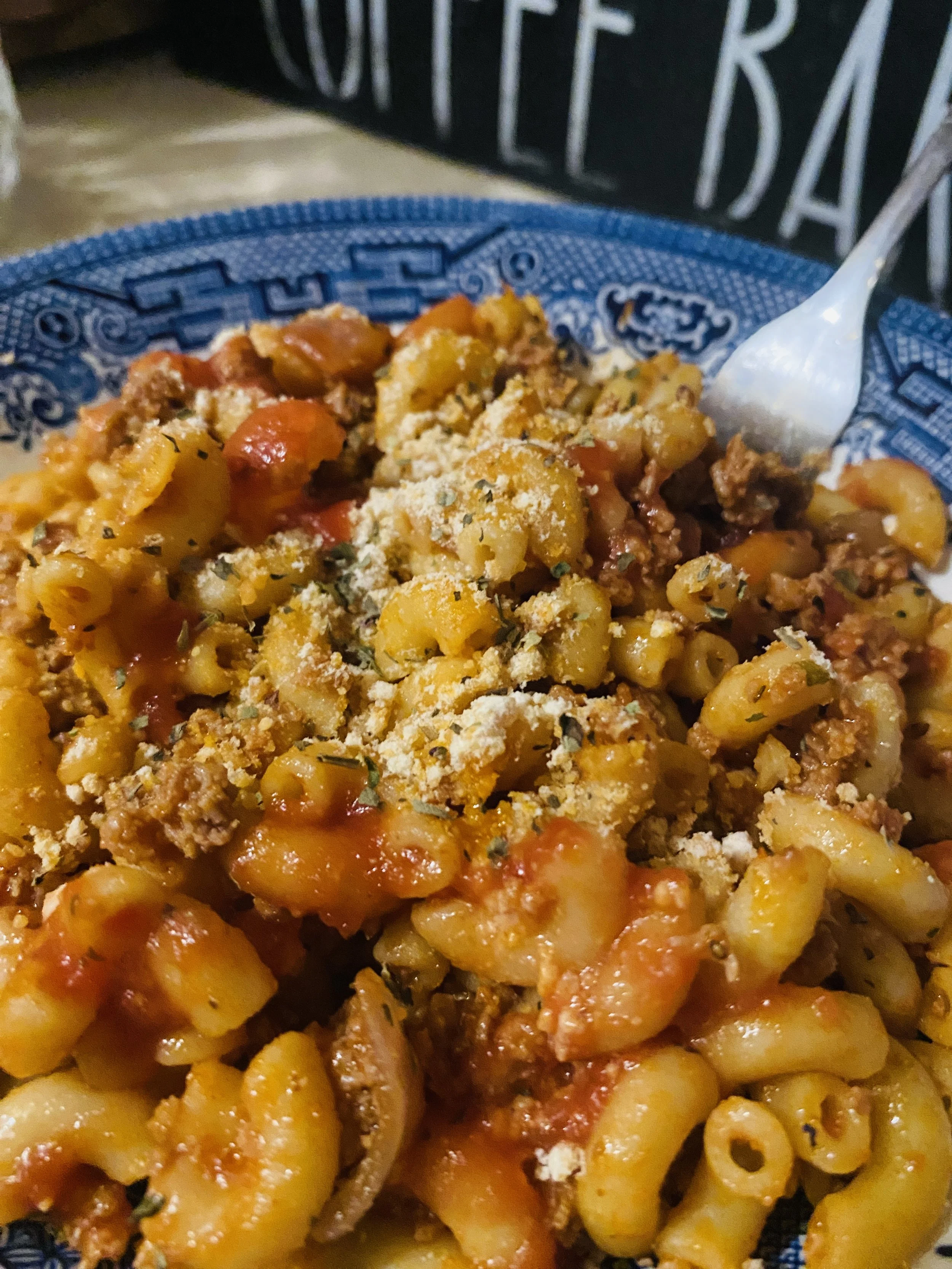 A bowl of Soul Macaroni Bolognese made with elbow macaroni coated in a rich, smoky meat sauce, topped with fresh basil and grated cheese.