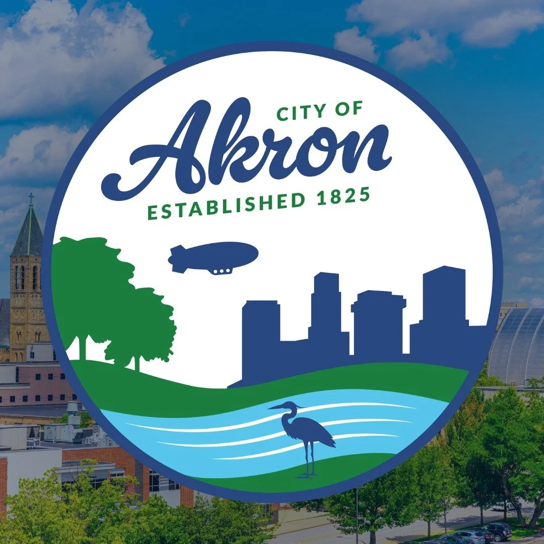 City of Akron logo featuring a city skyline, trees, a river, a heron, a blimp, and the text 'City of Akron Established 1825'