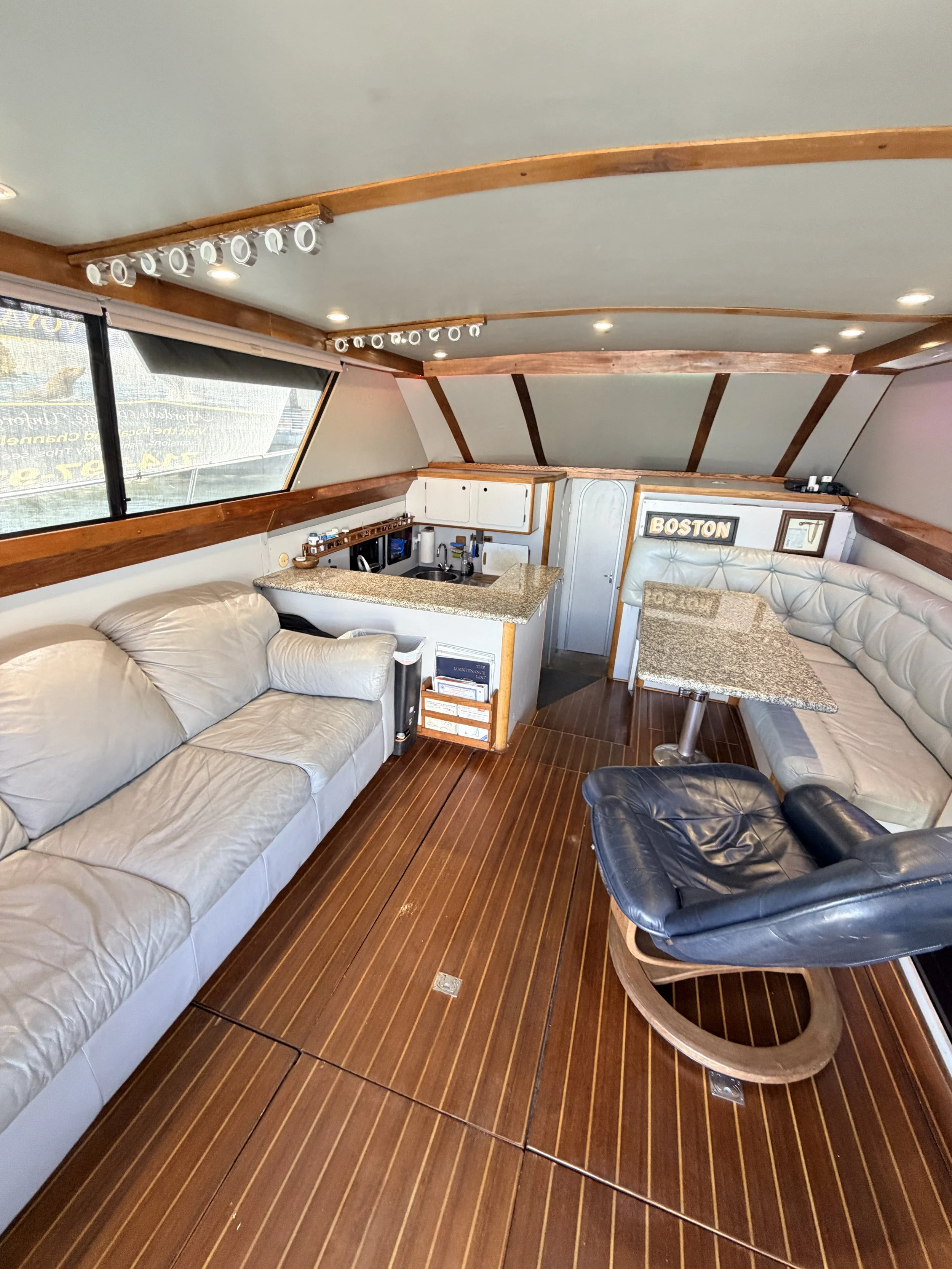 A navigation and fish finder screen mounted inside a boat with a sofa below, a small sign reading 'BOSTON,' and part of a granite countertop in the foreground.