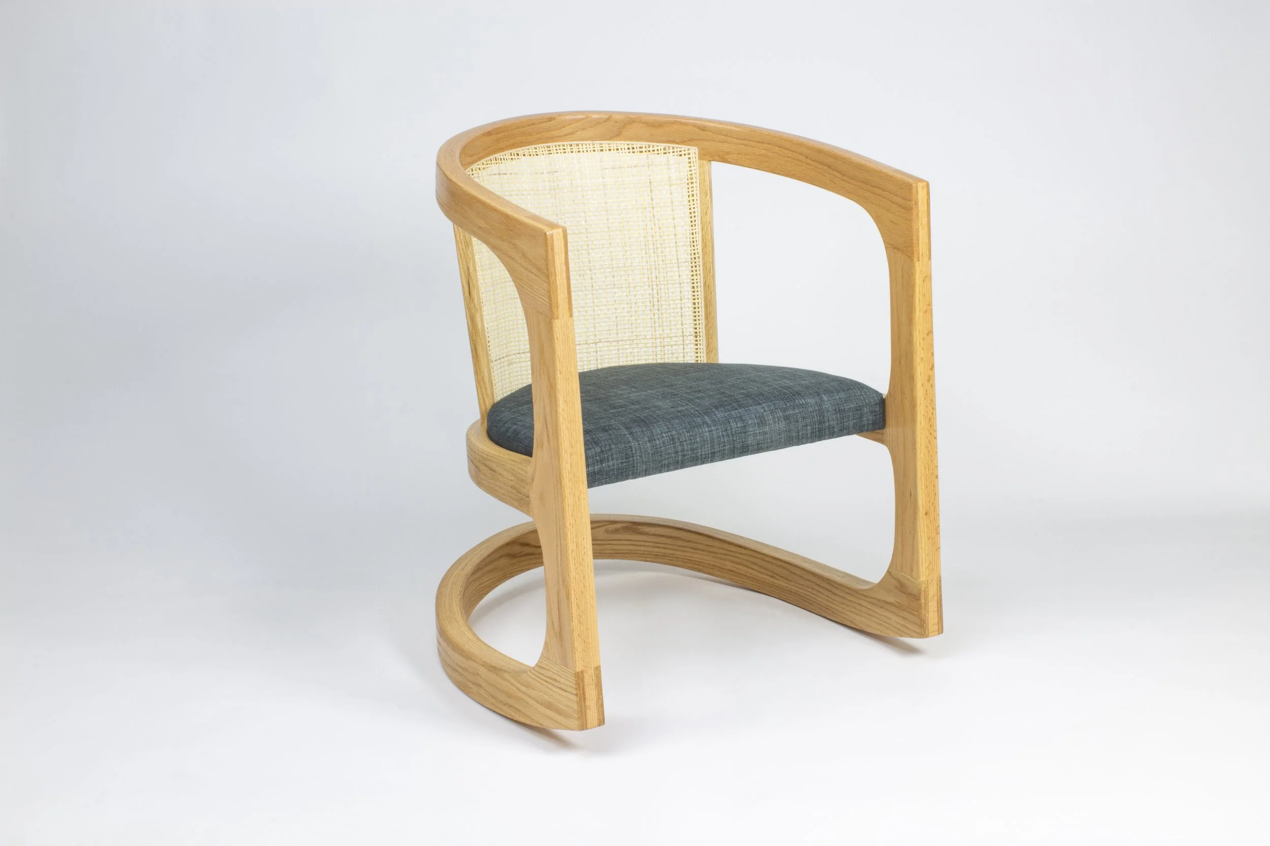 Modern wooden chair made of White Oak with a curved bent lamination frame, cane Swedish woven backrest, and dark blue fabric seat, placed against a plain white background.