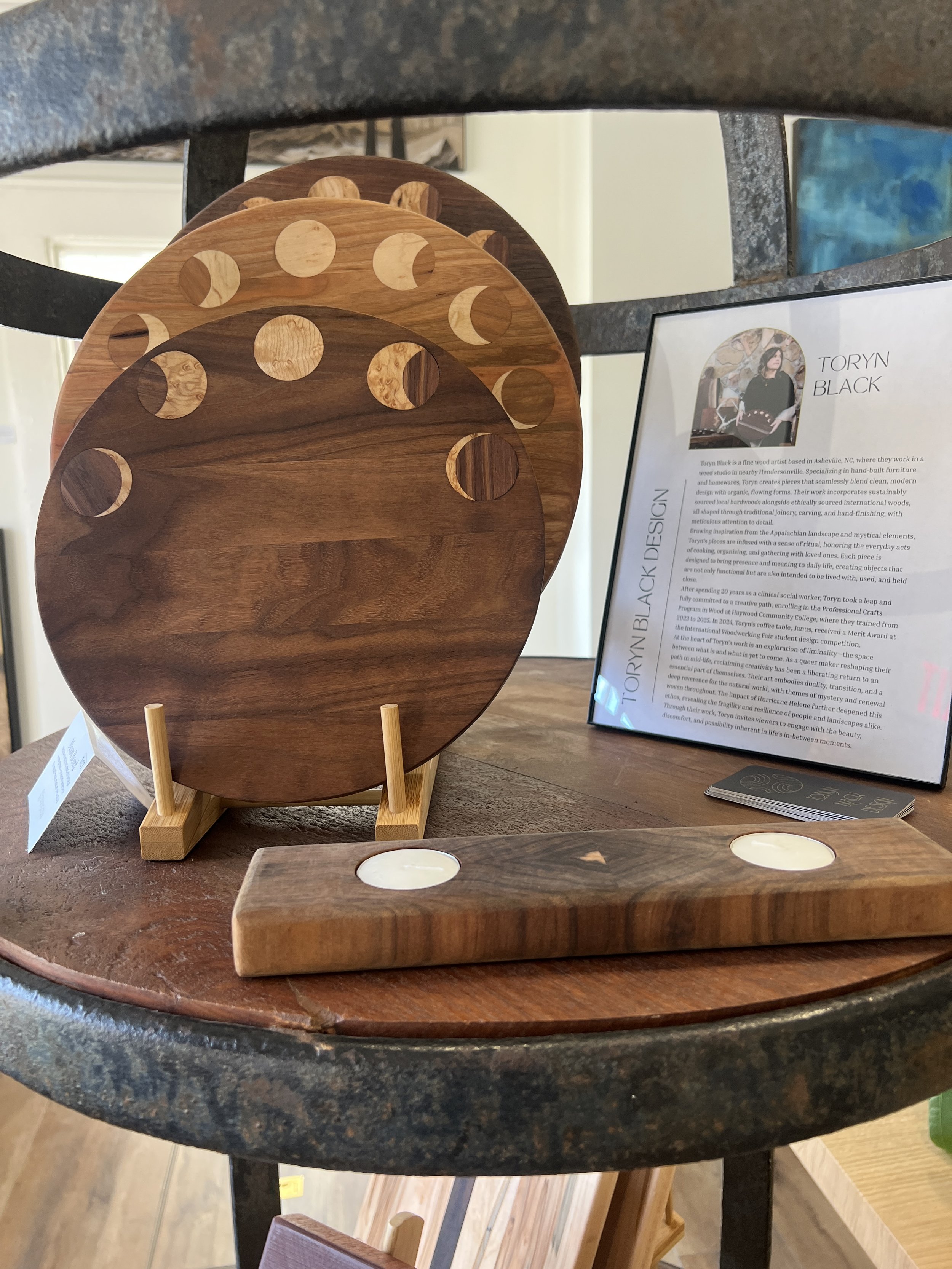 Toryn Black Design wooden homeware display with walnut and cherry serving boards, bird’s-eye maple moon phase inlays, and a Mansonia wood tea light holder with sapwood diamond pattern. To the left a a picture of Toryn Black with artist statement
