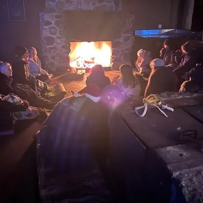 People sitting around a fireplace inside a rustic room.
