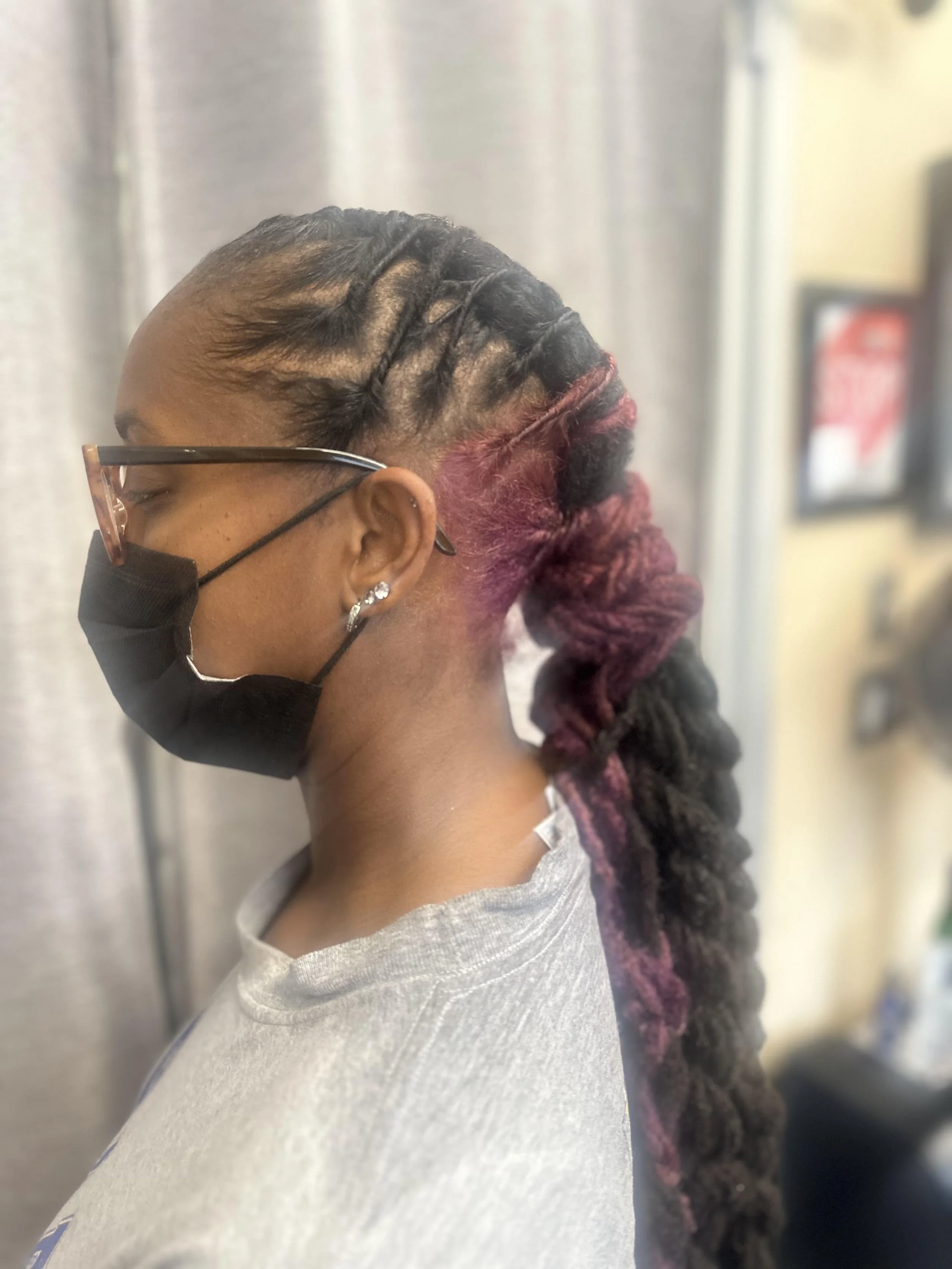 Side profile of a person with braided hair and a braided ponytail, wearing glasses and a black face mask.