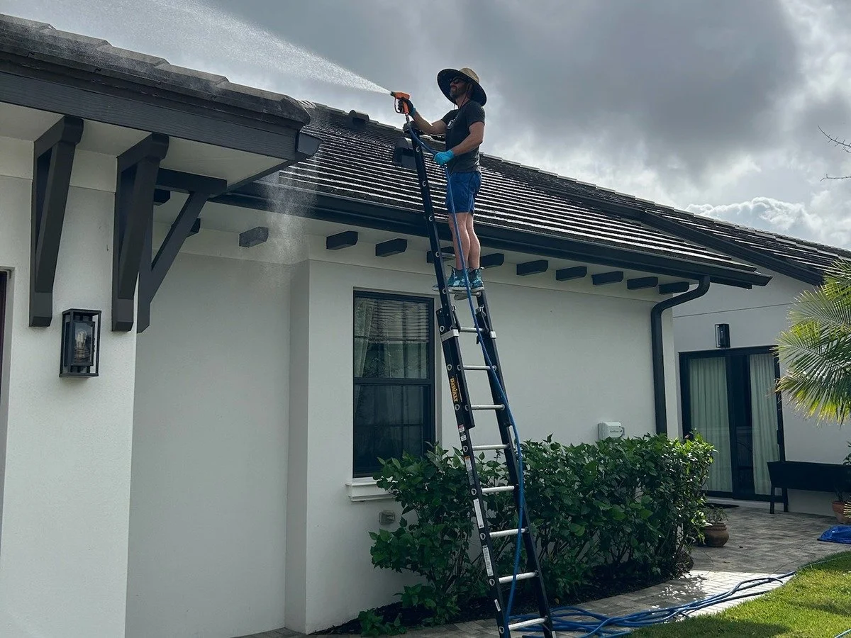 RAVE Power Wash technician on a ladder soft washing the roofline of a white stucco home
