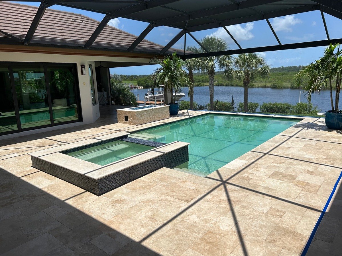 Clean travertine pool deck and spa inside a screened lanai overlooking the water in Sarasota, FL