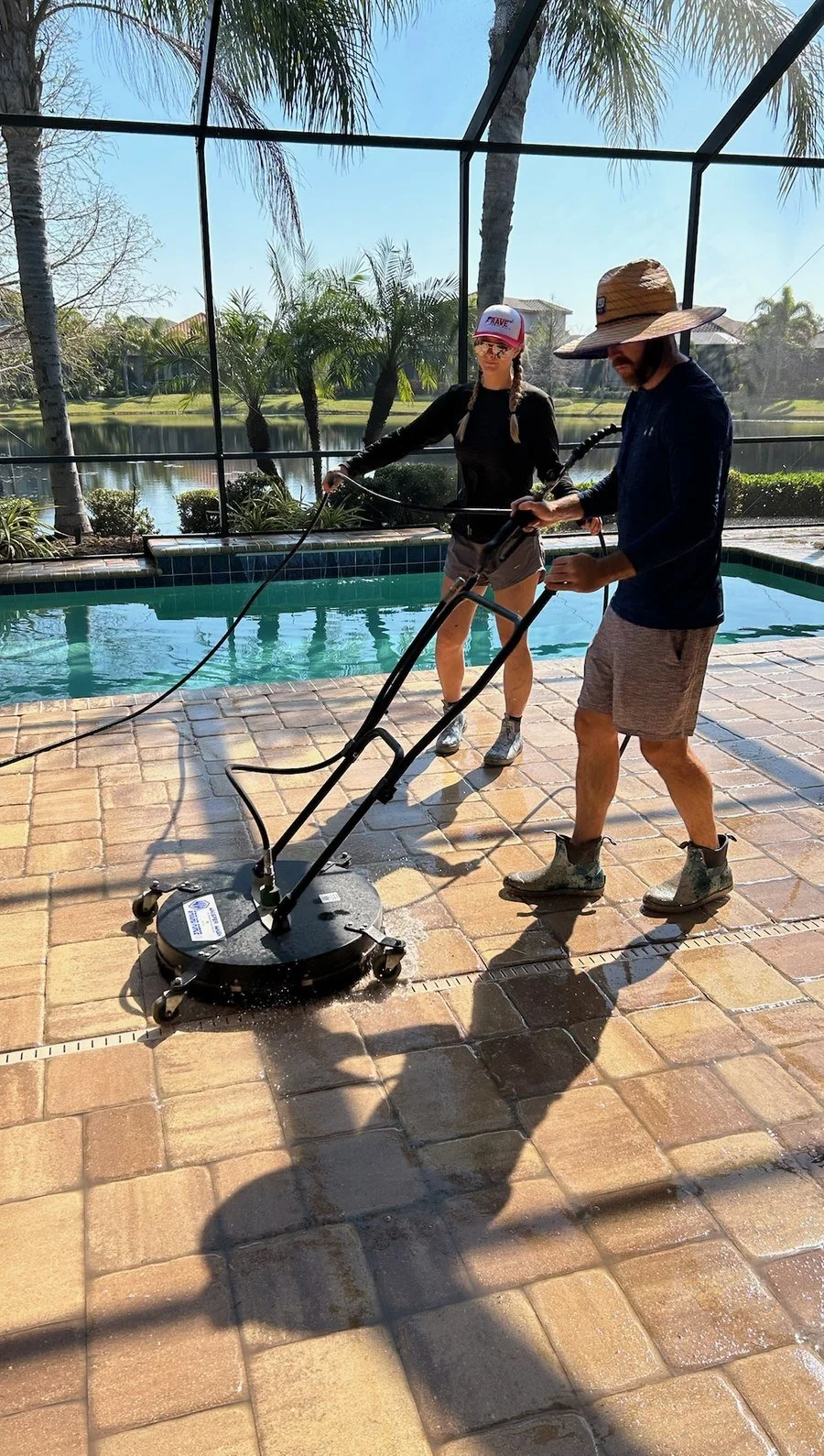 Technician pressure washing a screened lanai overlooking a lake and golf course