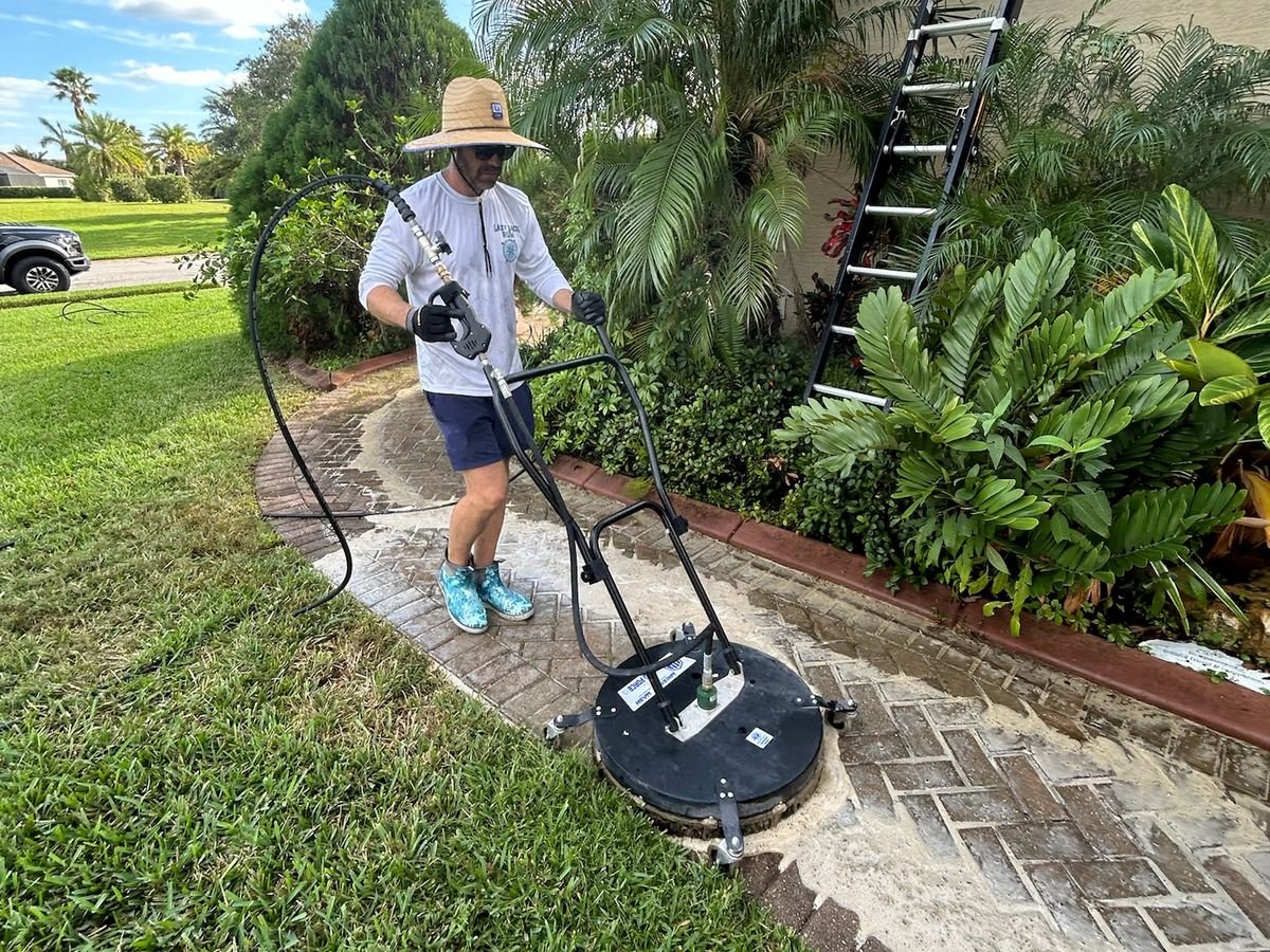 Technician using a surface cleaner on a brick paver walkway beside a house