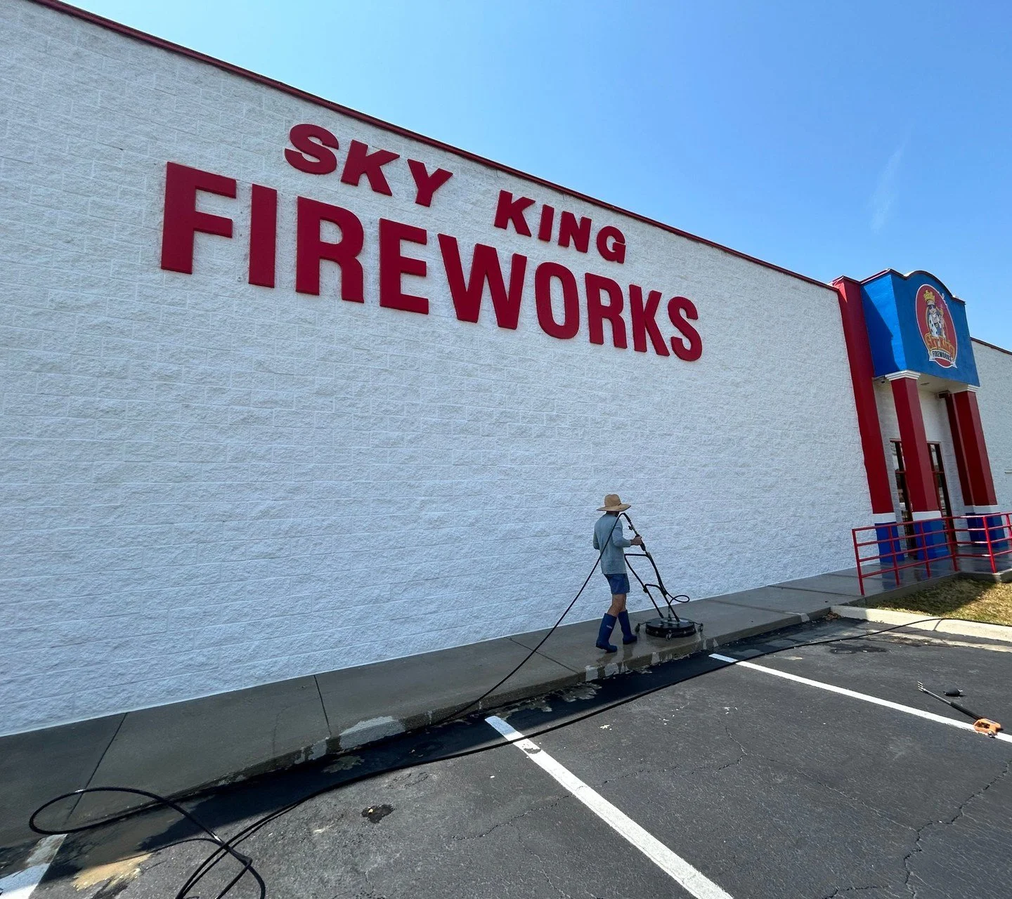 Technician pressure washing the sidewalk along a large white commercial building