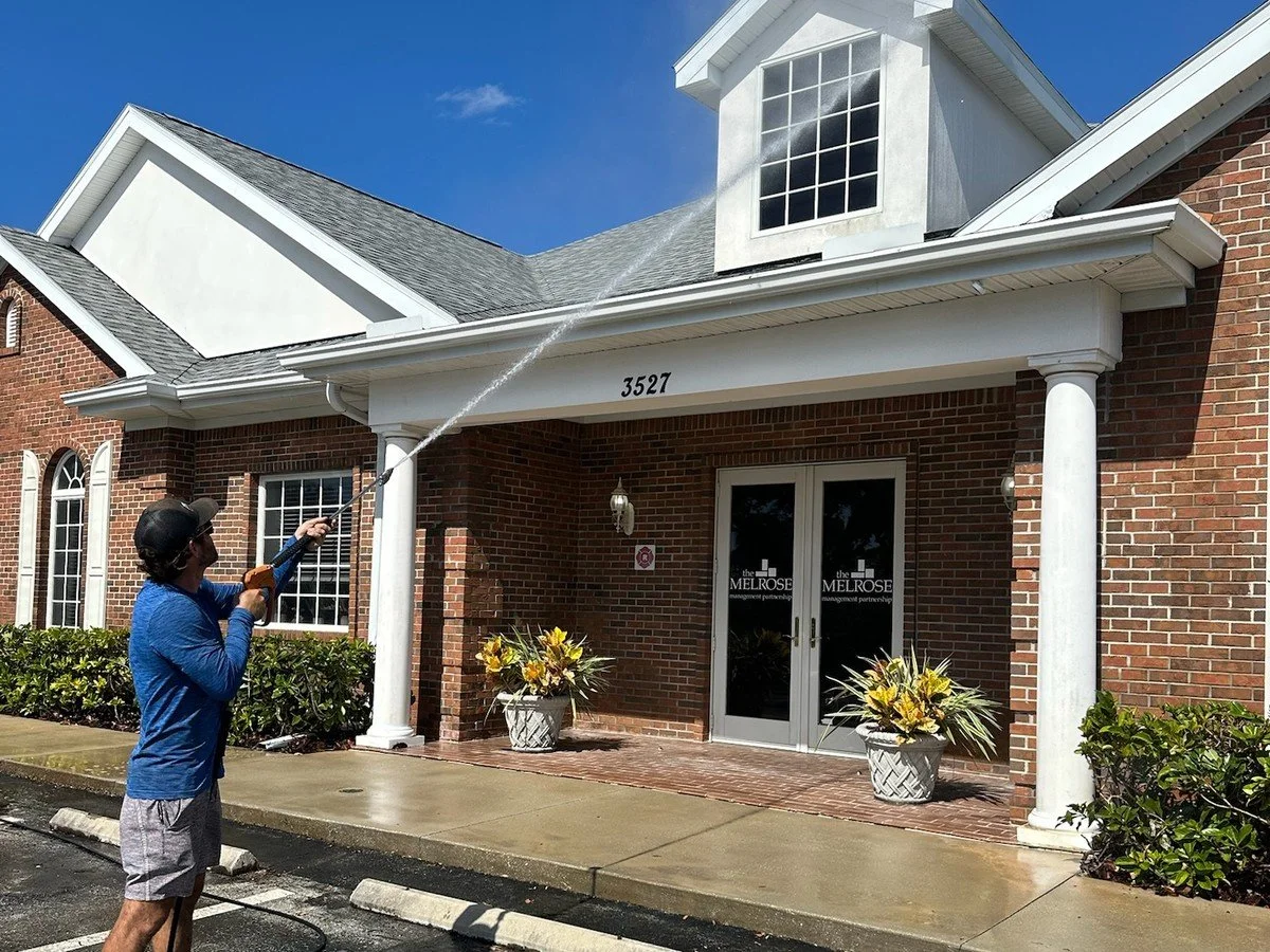 Technician soft washing the stucco dormer and roofline of a brick office building