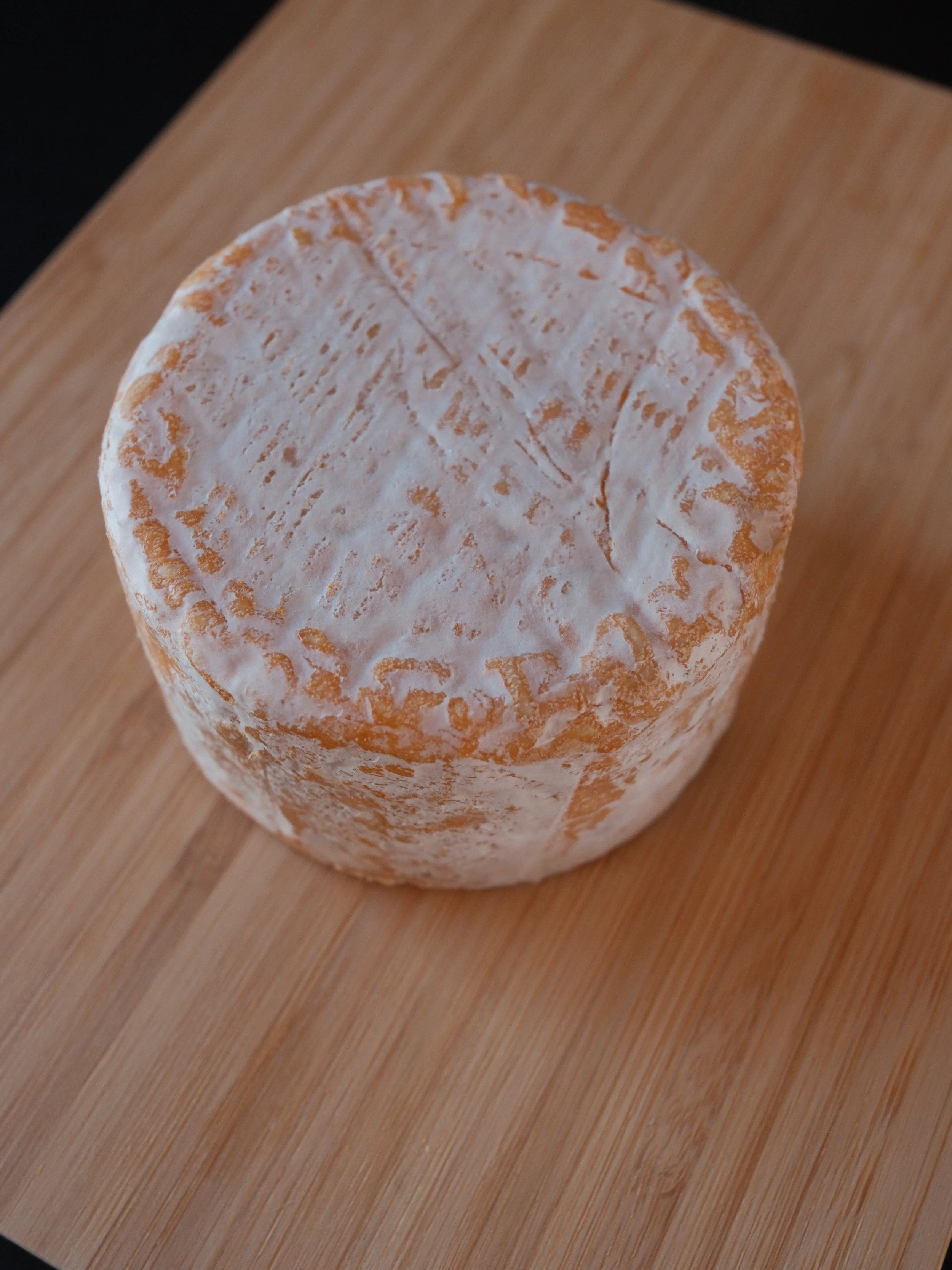 A wheel of brie cheese with a white rind, resting on a wooden surface.
