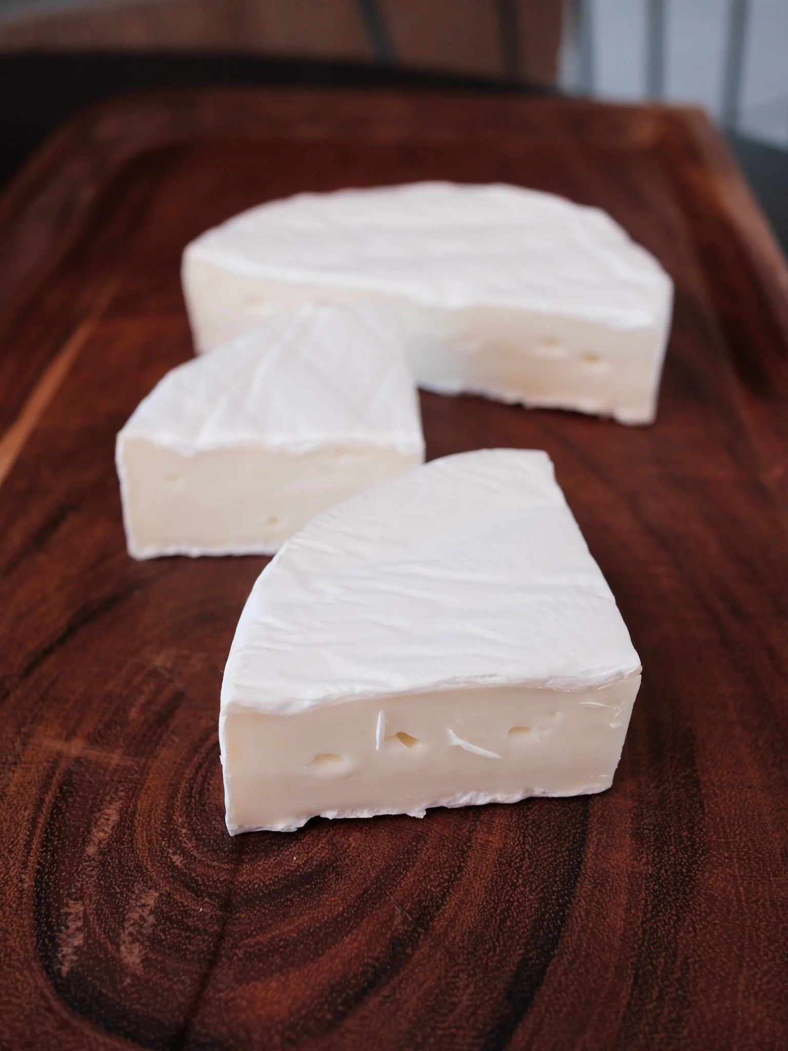 a piece of camembert by la bonne vie sits on a dark wood board