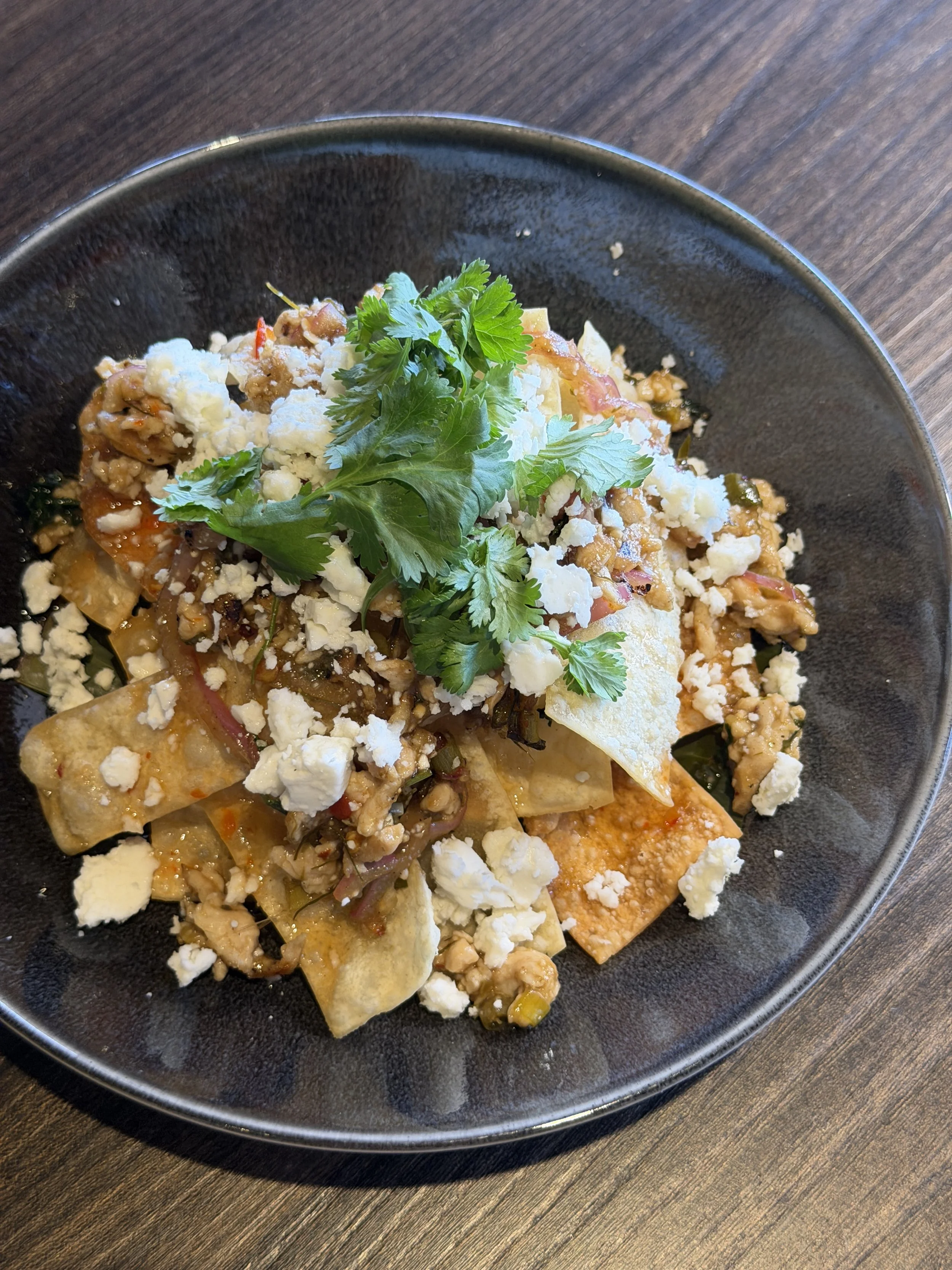 thai larb nachos with fresh feta and cilantro on a black plate