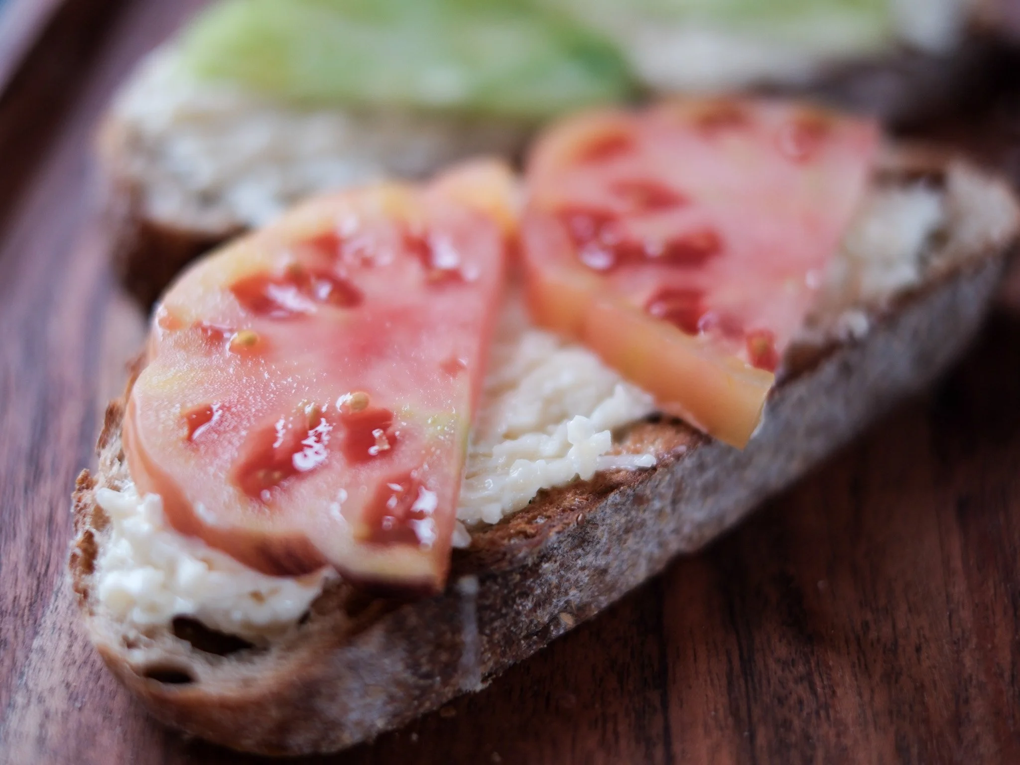 two pieces of toast with fresh red and green tomatoes lay on a bed of creamy cheese and mayo