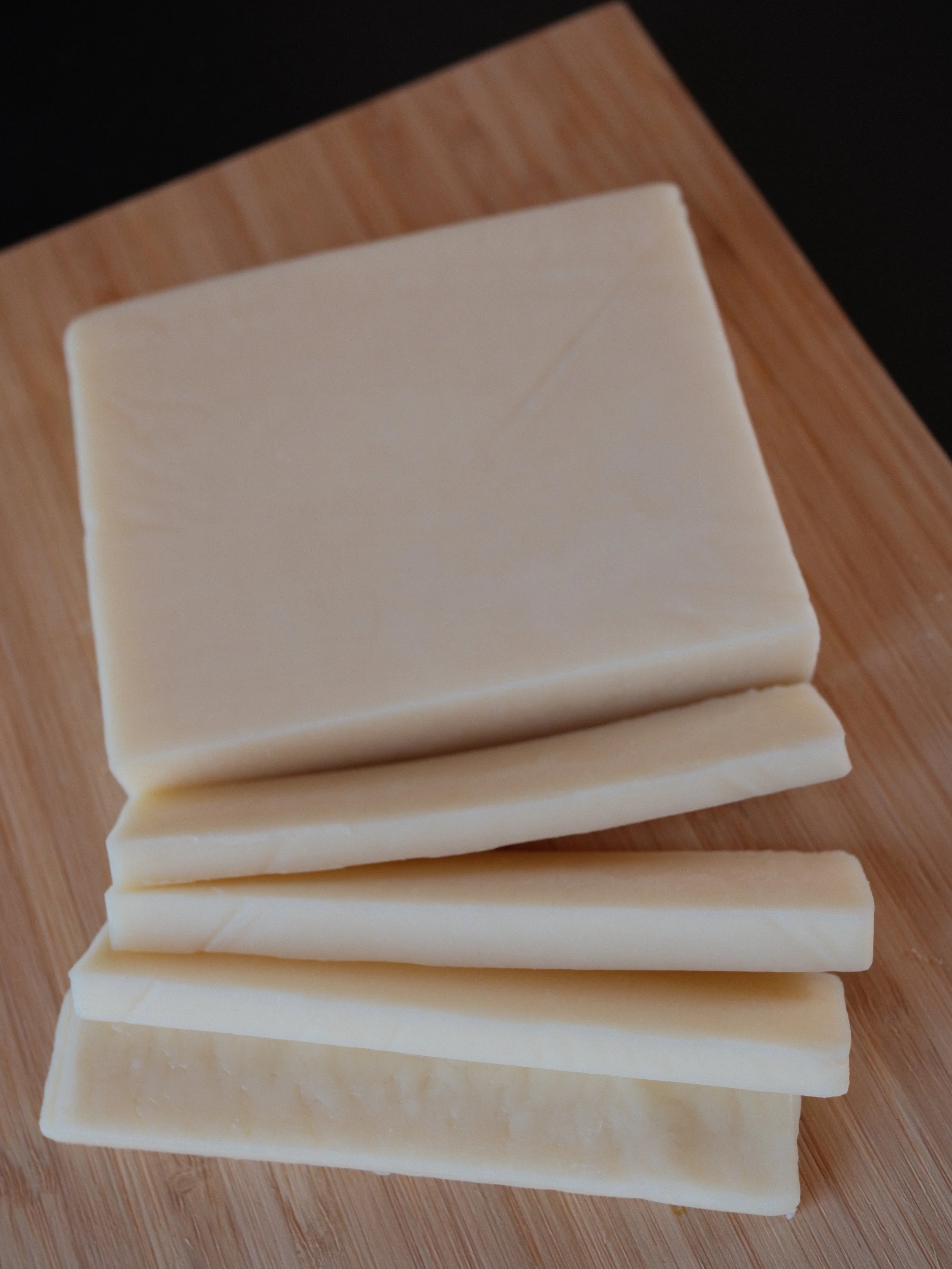 Slices of different types of cheese on a wooden cutting board.