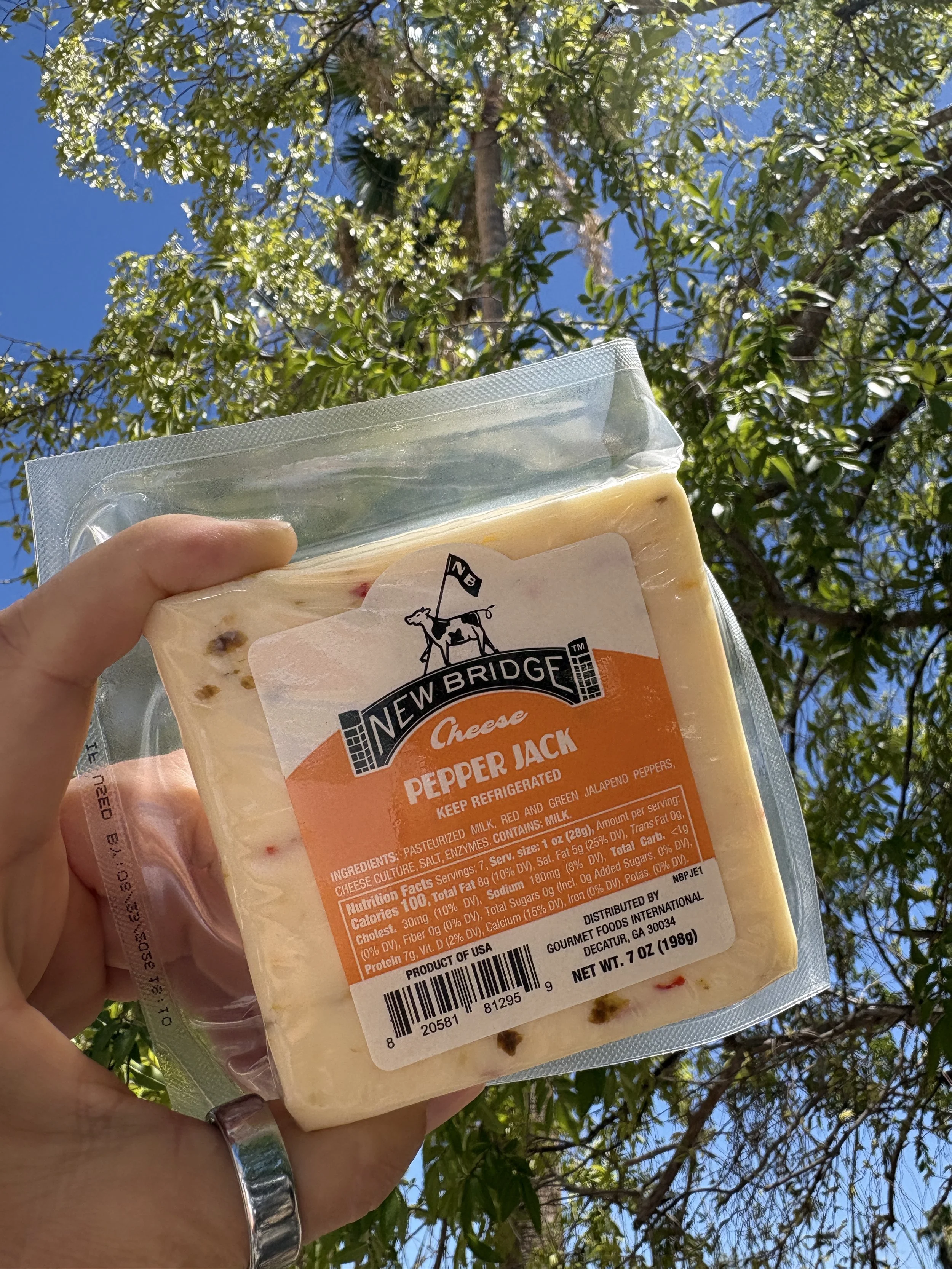 A hand holds a block of New Bridge Pepper Jack cheese up to the sky