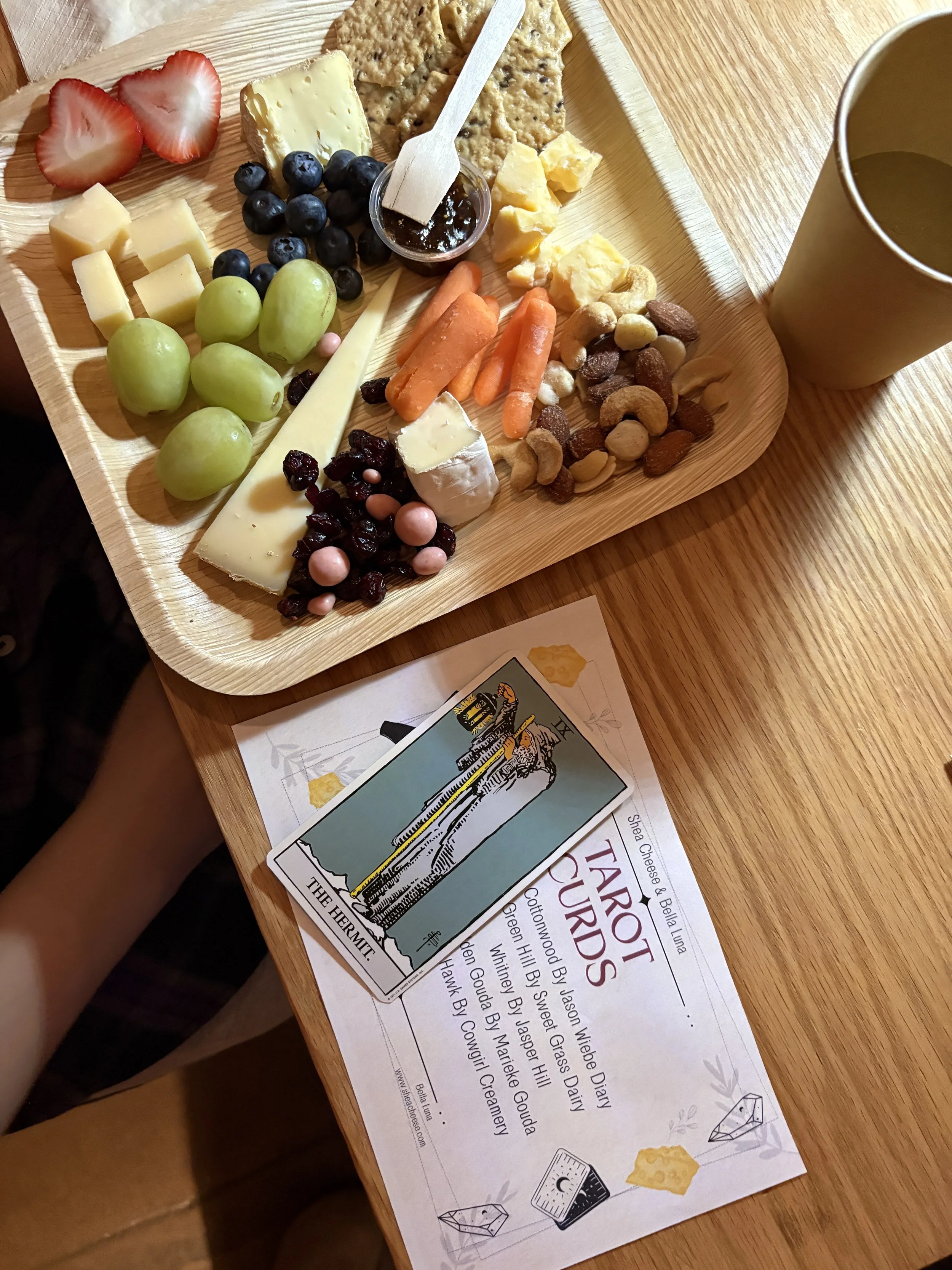 a cheese plate with several kinds of cheese, fruit, and nuts with tarot card on the side.