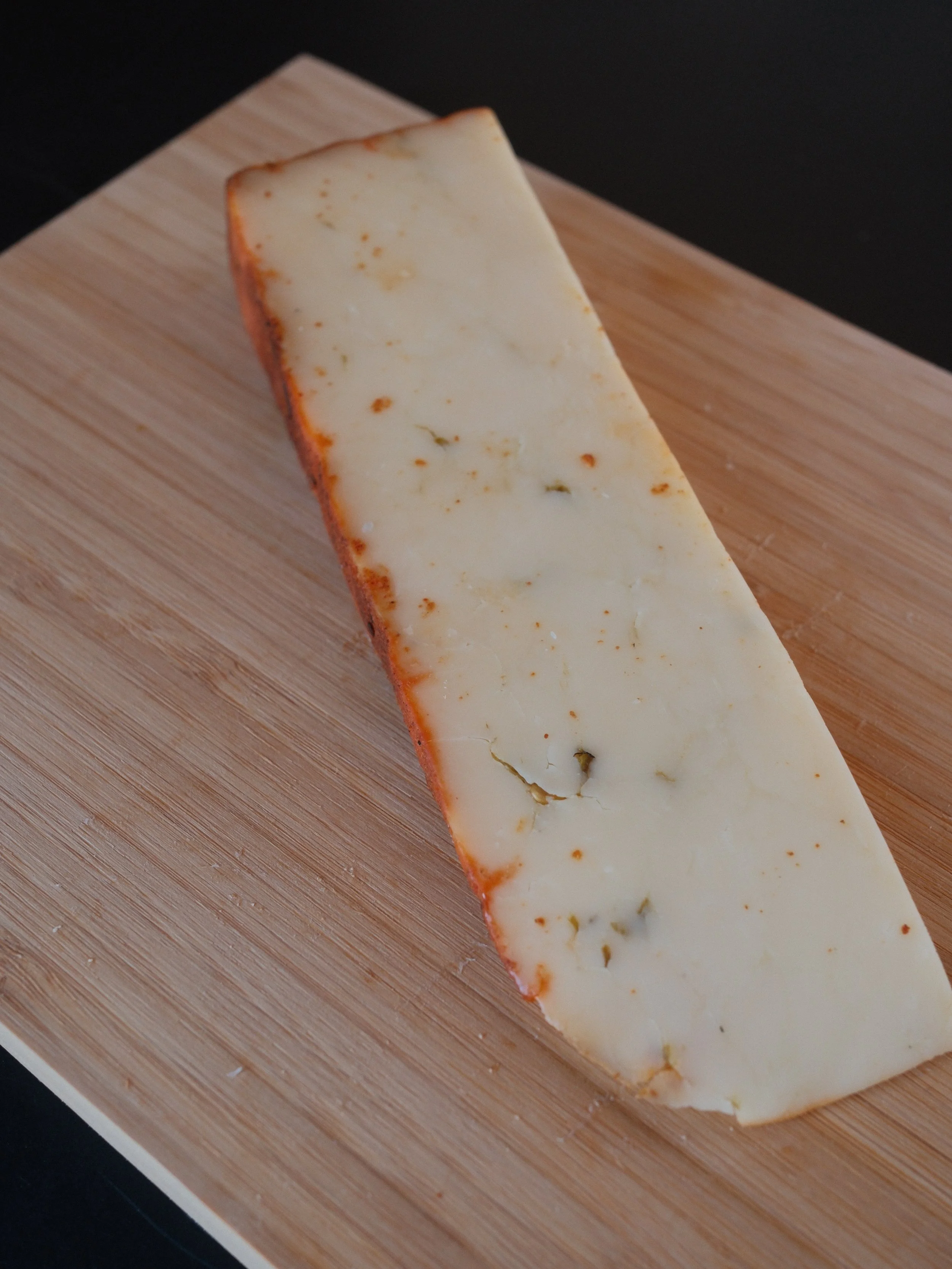A wedge of white cheese with a brown rind on a light wooden board.