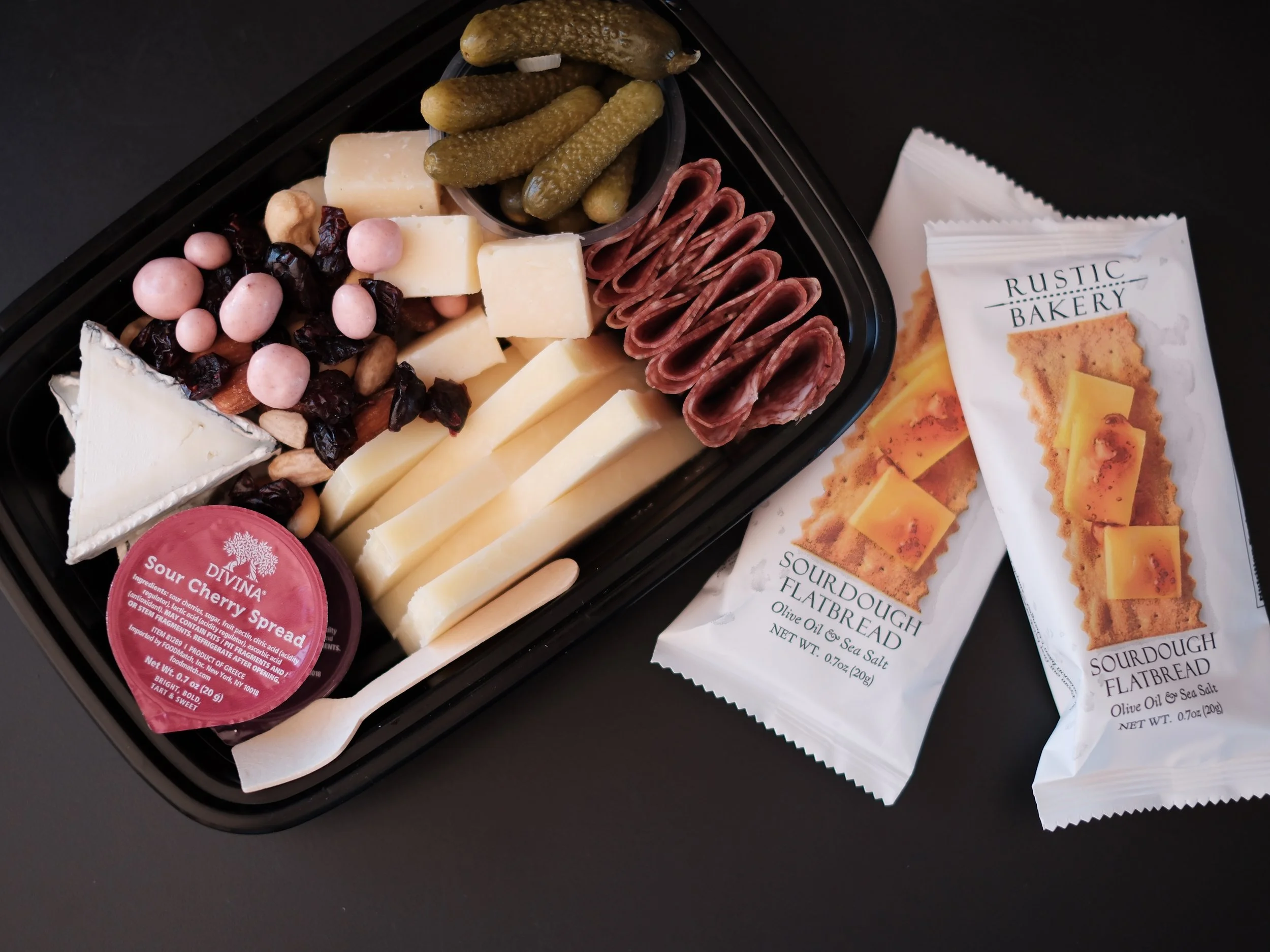 a to go box filled with cheese, jam, meat, pickles, nuts, and dried fruit.