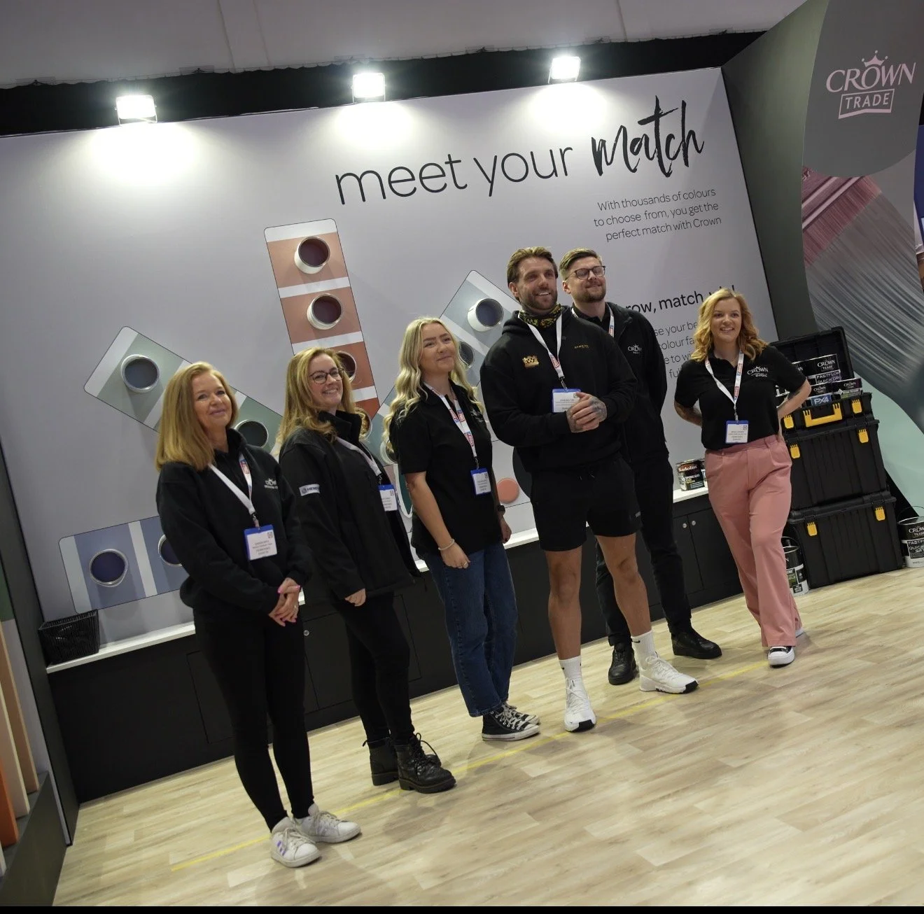 Group of six people standing in front of a display at a trade show or exhibition, with a sign that reads 'meet your match' and colorful paint sample displays in the background.