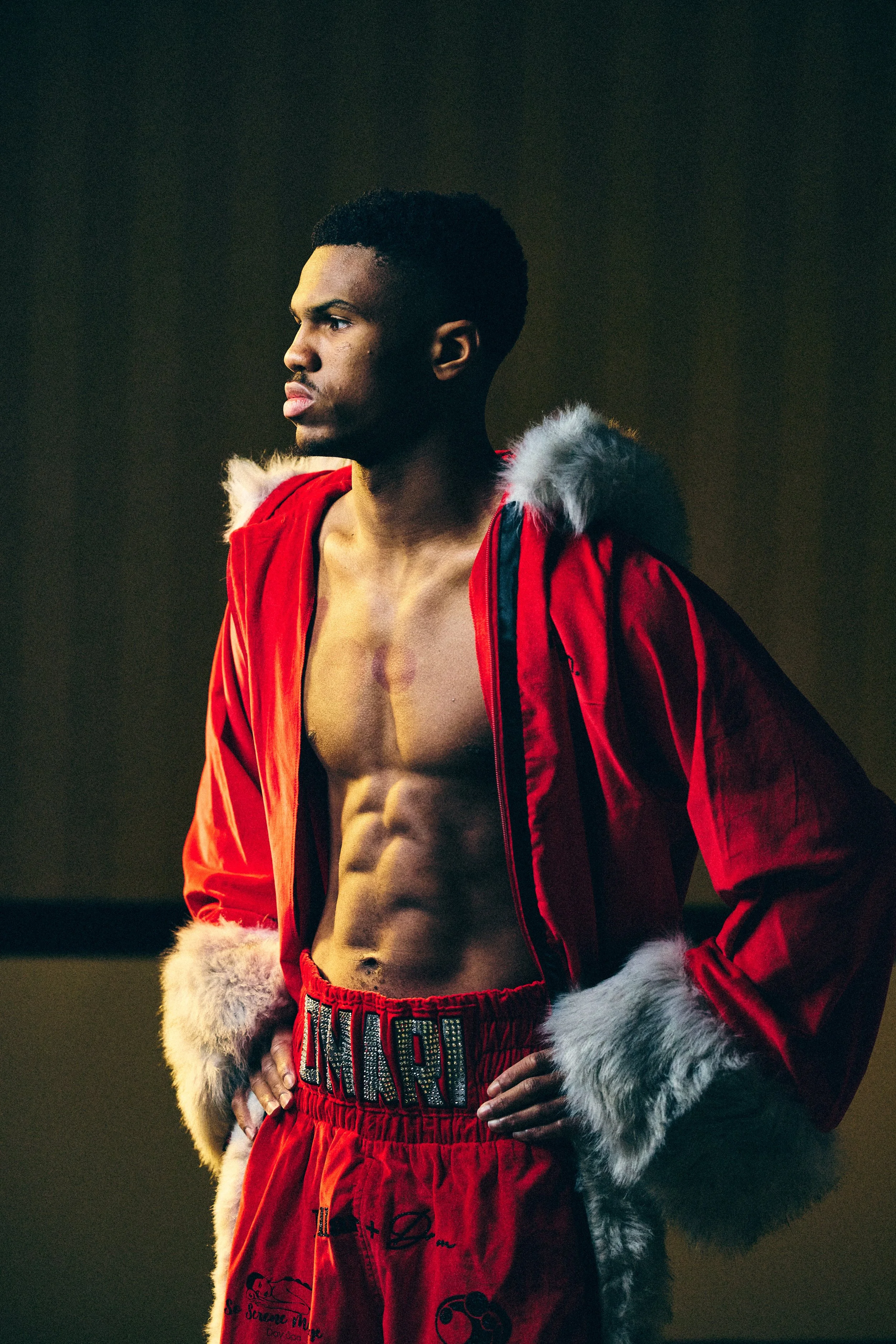A young man sitting on the floor of a boxing gym, holding up a gold medal with a blue ribbon, after a match or competition.