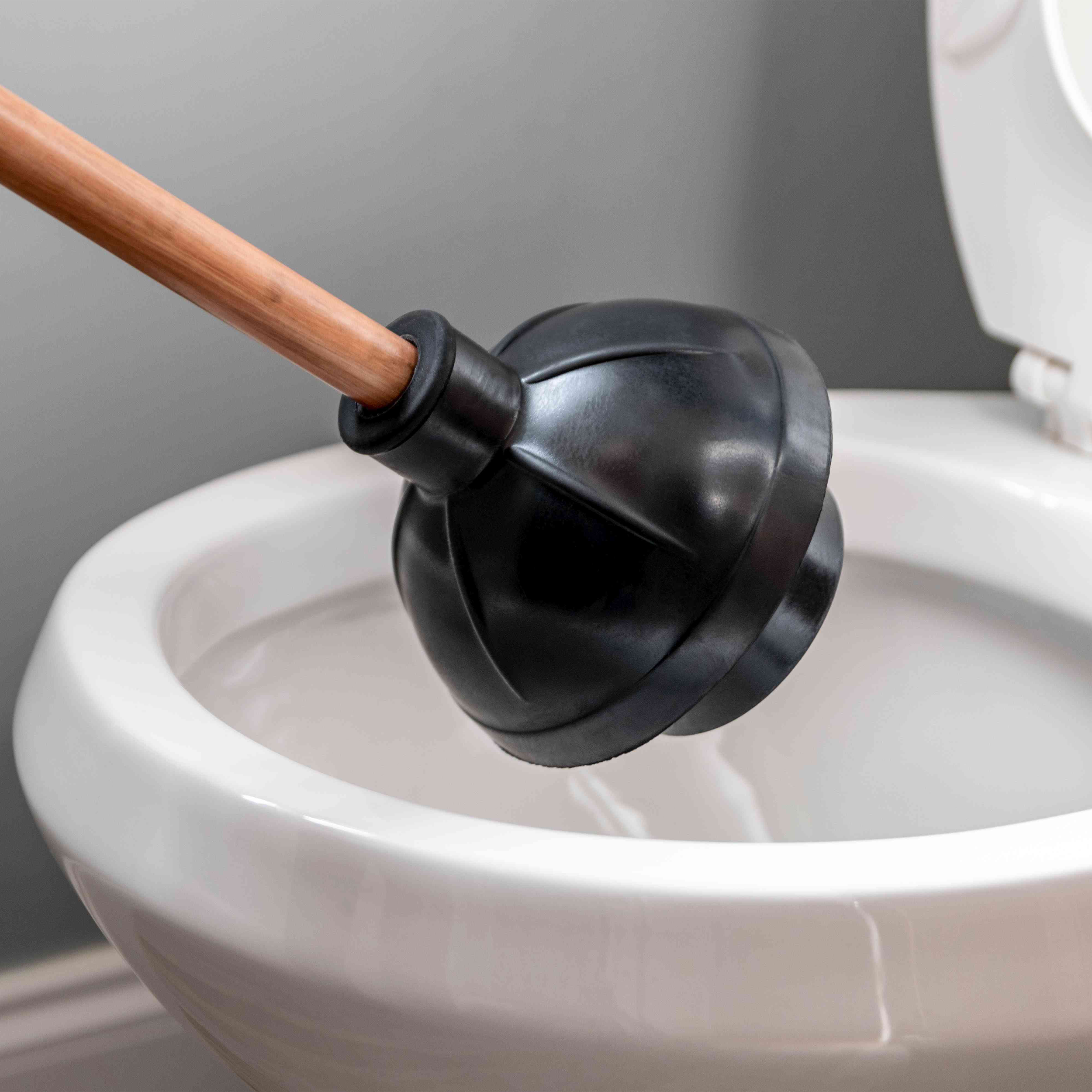 A toilet plunger with a wooden handle is positioned inside a white ceramic toilet bowl.