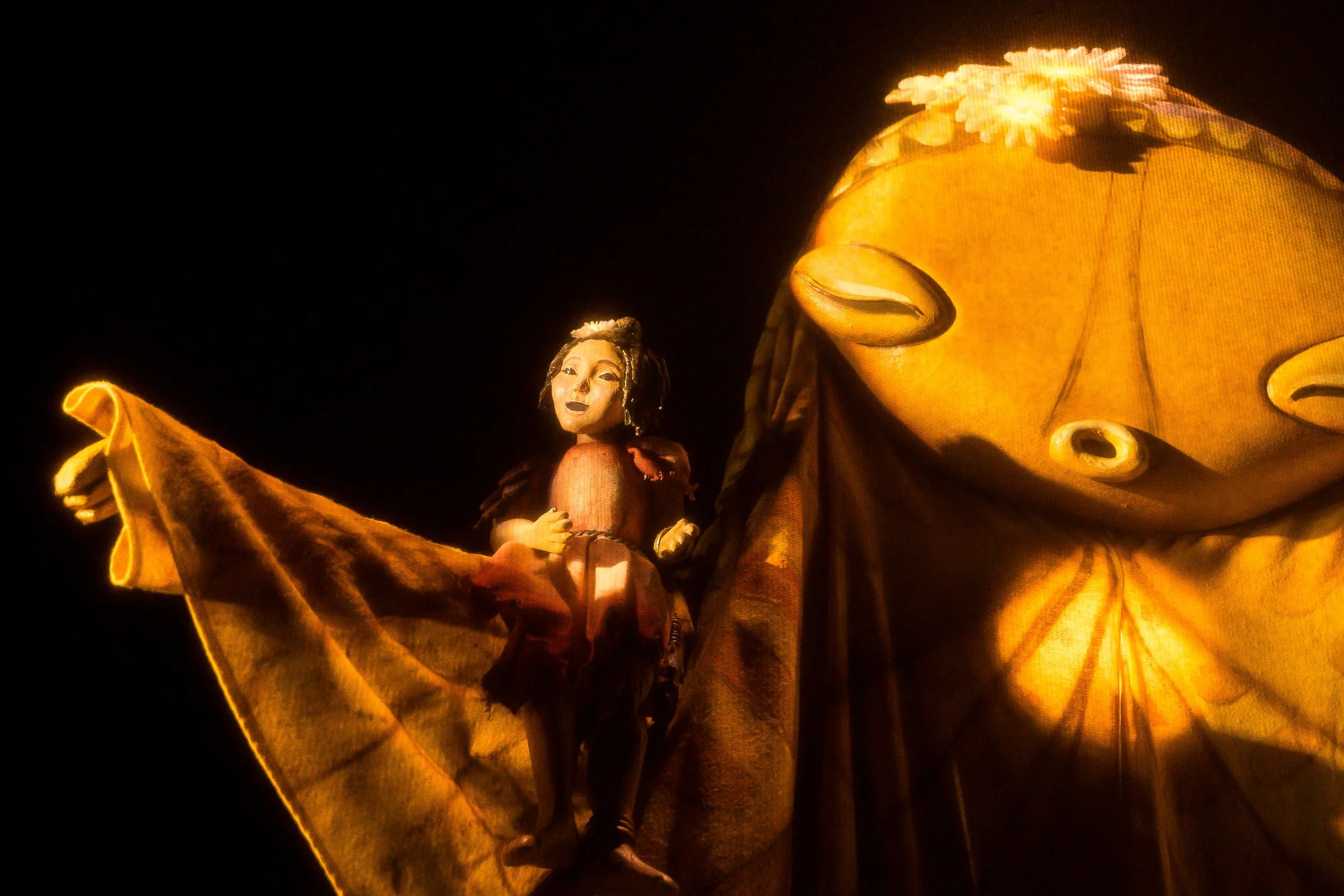 A brightly lit puppet display featuring a human figure riding on the back of a large, glowing insect or moth with detailed wings and antennae.