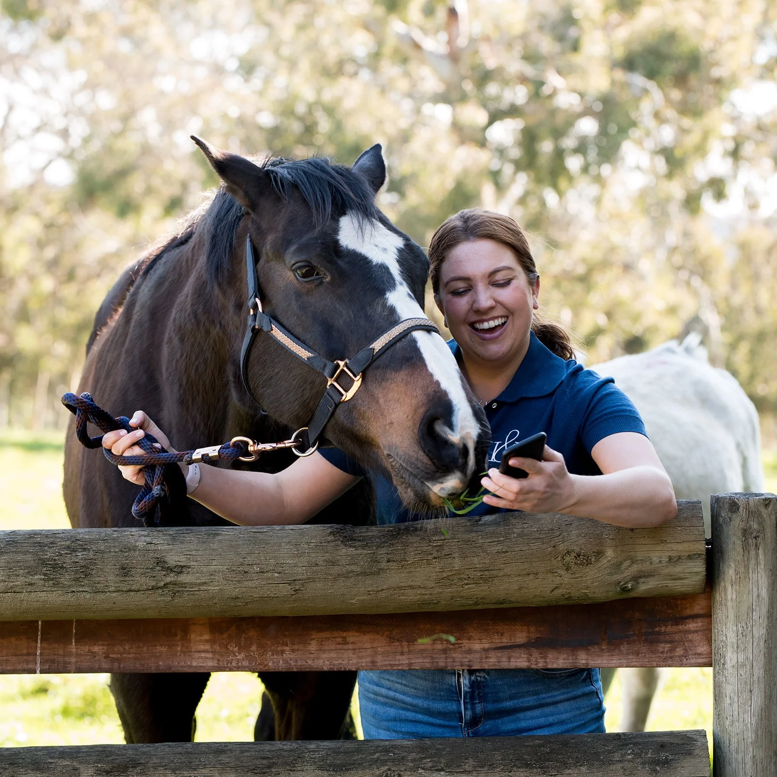 A woman looks at her phone smiling with green pastures in the background.