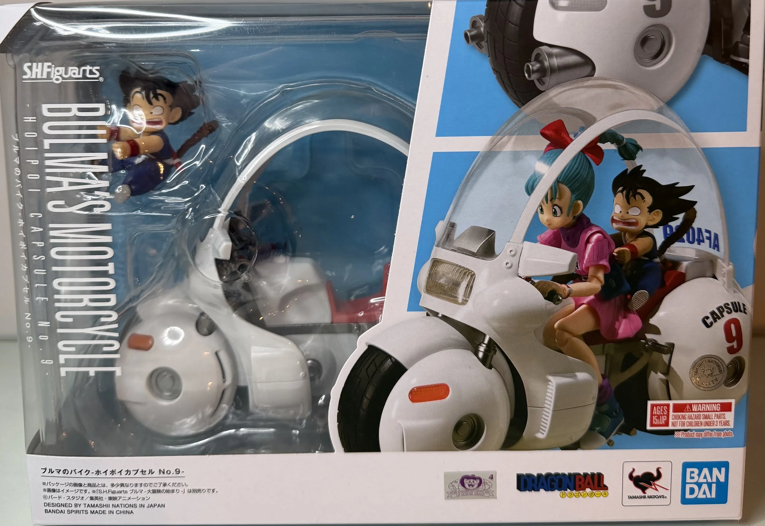 A Dragon Ball Z capsule toy set featuring Bulma and Goku riding a white motorcycle. The packaging shows an illustration of the toy outside the box.