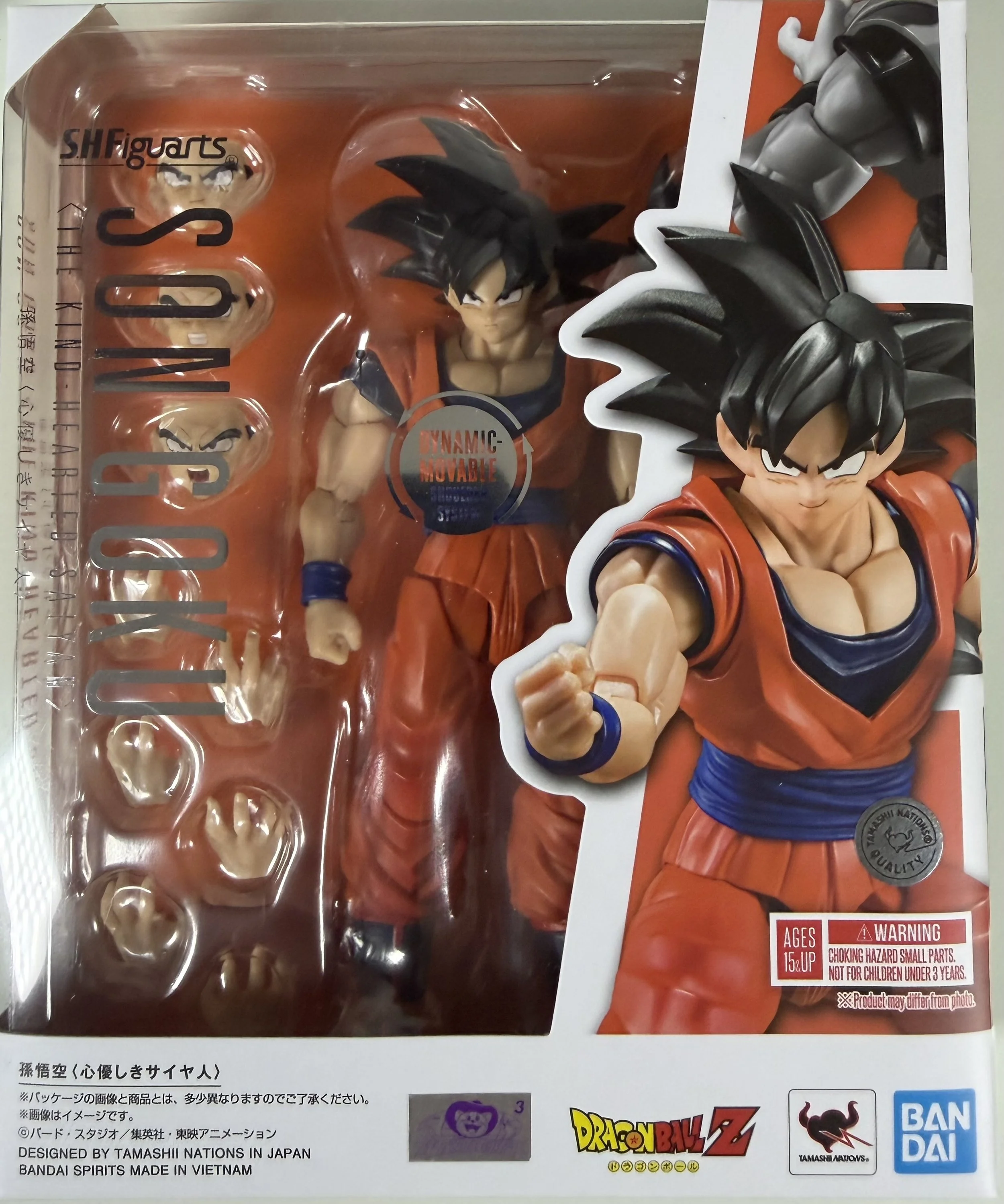 A Dragon Ball Z action figure of Goku in an orange and blue outfit, with spiky black hair and a fighting stance, inside a plastic packaging with thematic artwork and logos, including Bandai and Tamashii Nations branding.