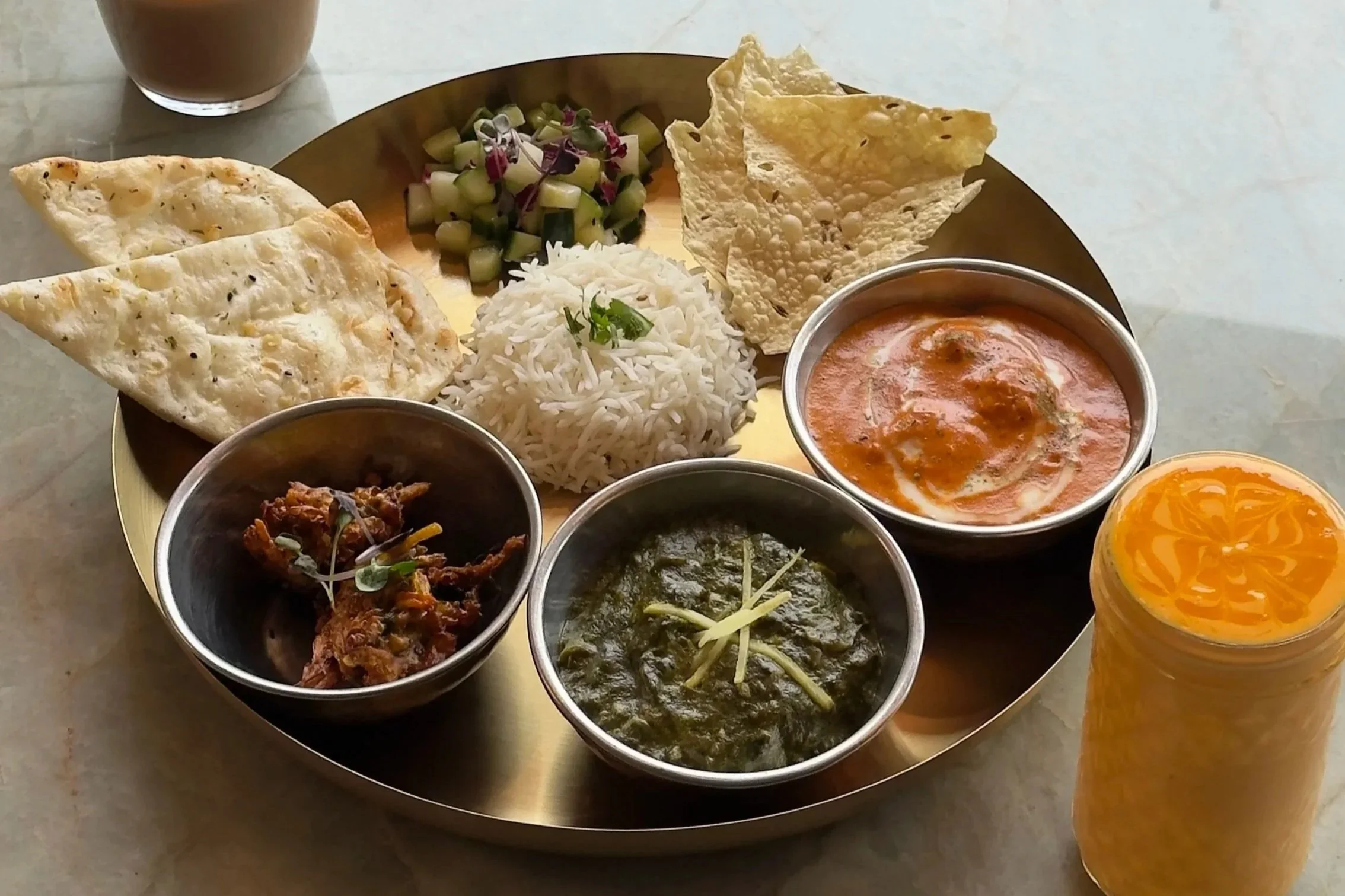 A traditional Indian thali with various dishes including rice, curries, chapati, papad, salad, pickle, and a fruit drink.