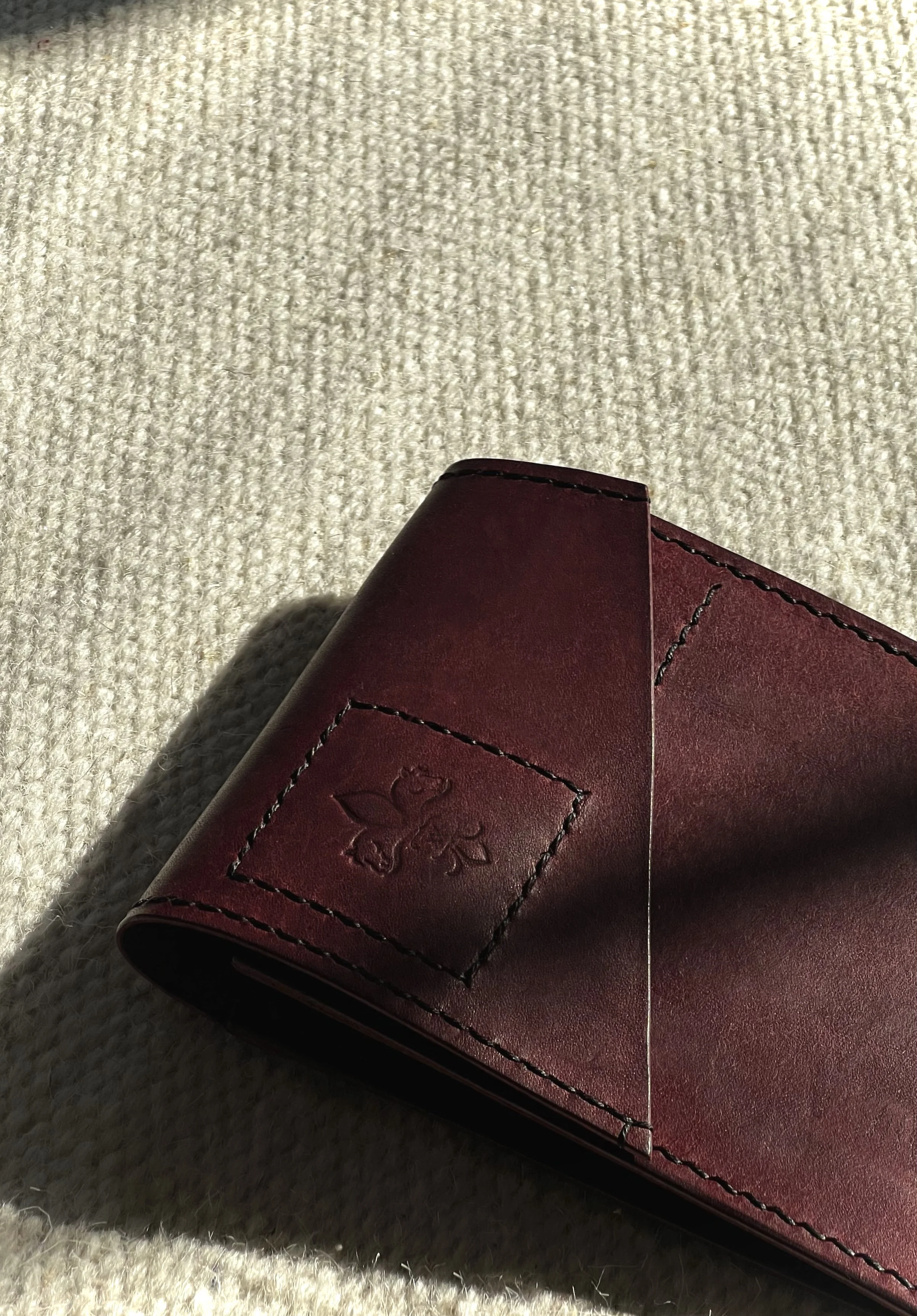 Rote Lederbrieftasche mit eingestanztem Logo liegt auf einer hellen, texturierten Oberfläche.