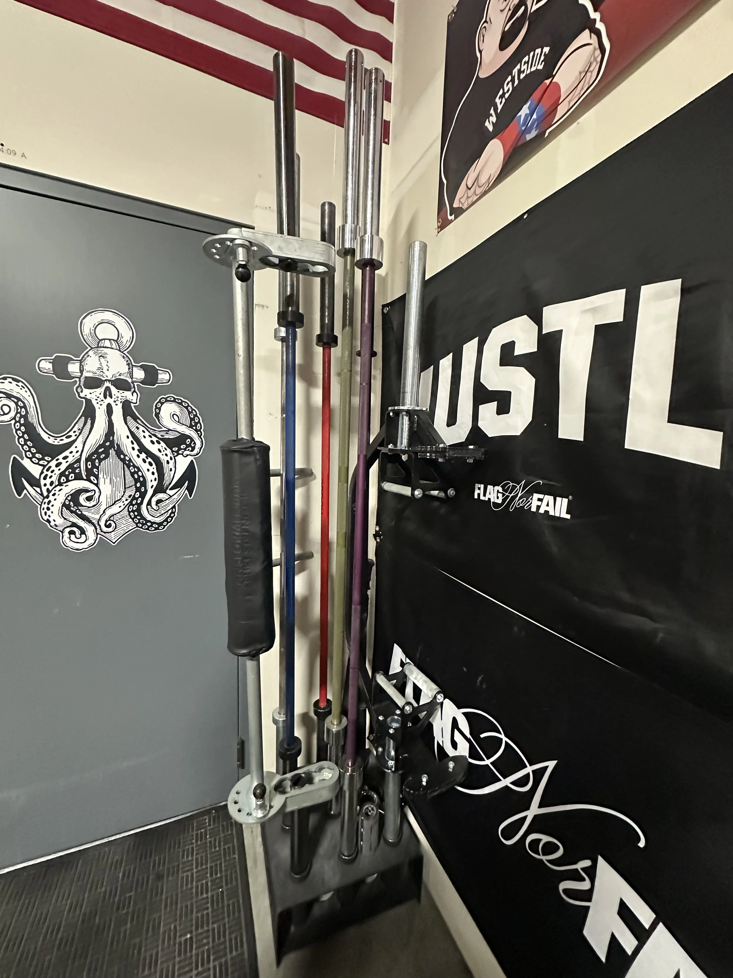 A set of weightlifting bars and plates stored vertically in a corner, with wall decals including a black banner.
