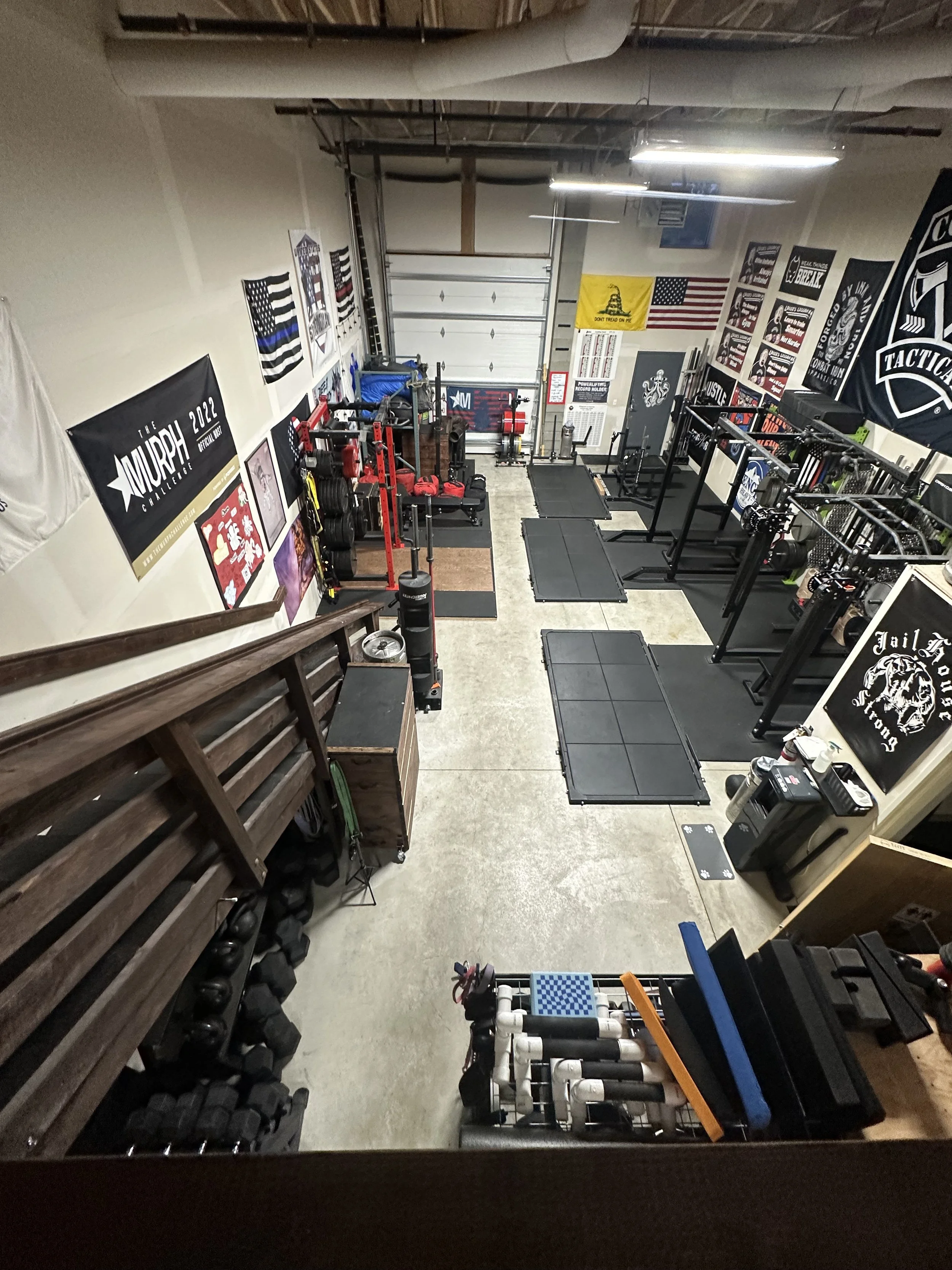 Gym with weightlifting equipment, banners, flags, and workout mats arranged along the walls.