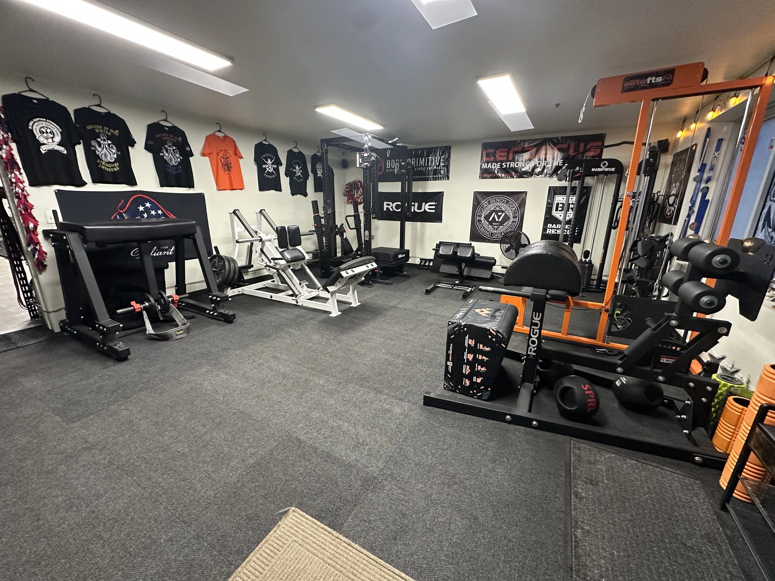 A gym workout room with various exercise equipment, wall banners, T-shirts hanging on the wall, and weights on the racks.