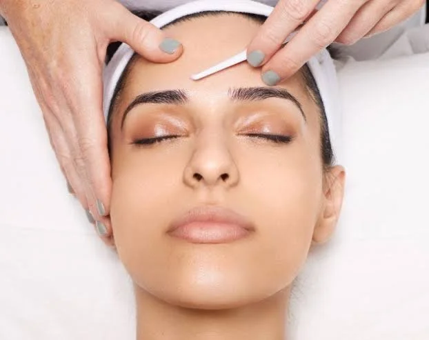 A woman receiving a face treatment with a dermaplaning tool.