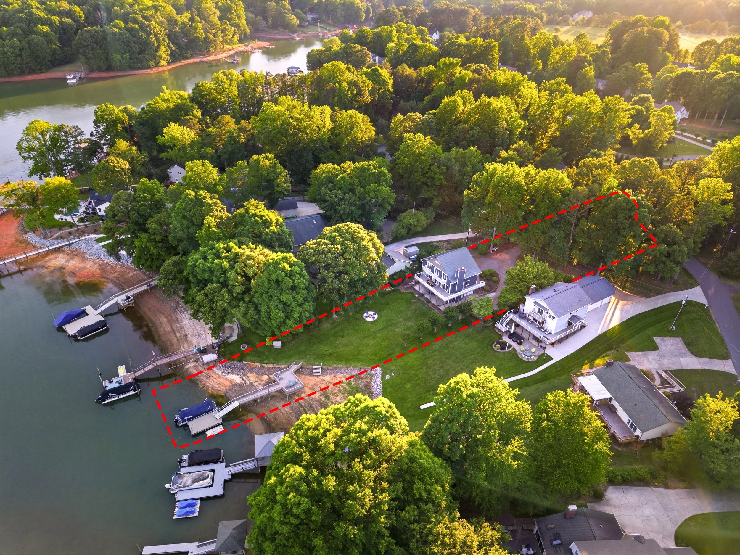 Aerial view of waterfront property outlined in red, featuring two houses, docks, driveways, and surrounding trees along a lakeshore.