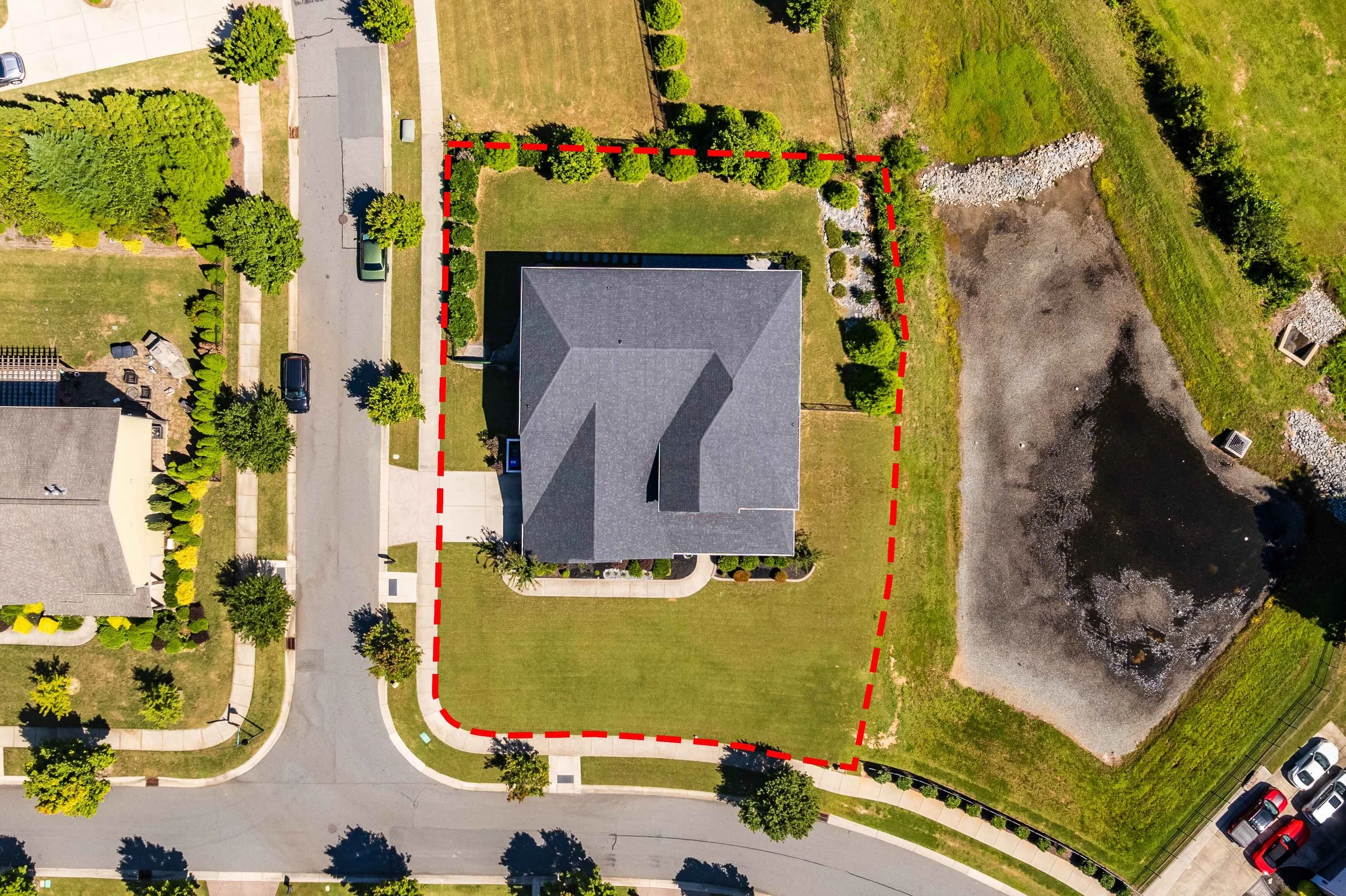 Aerial view of a residential neighborhood featuring a house with a gray roof, outlined by a red dashed line. Surrounding green lawns and streets are visible.